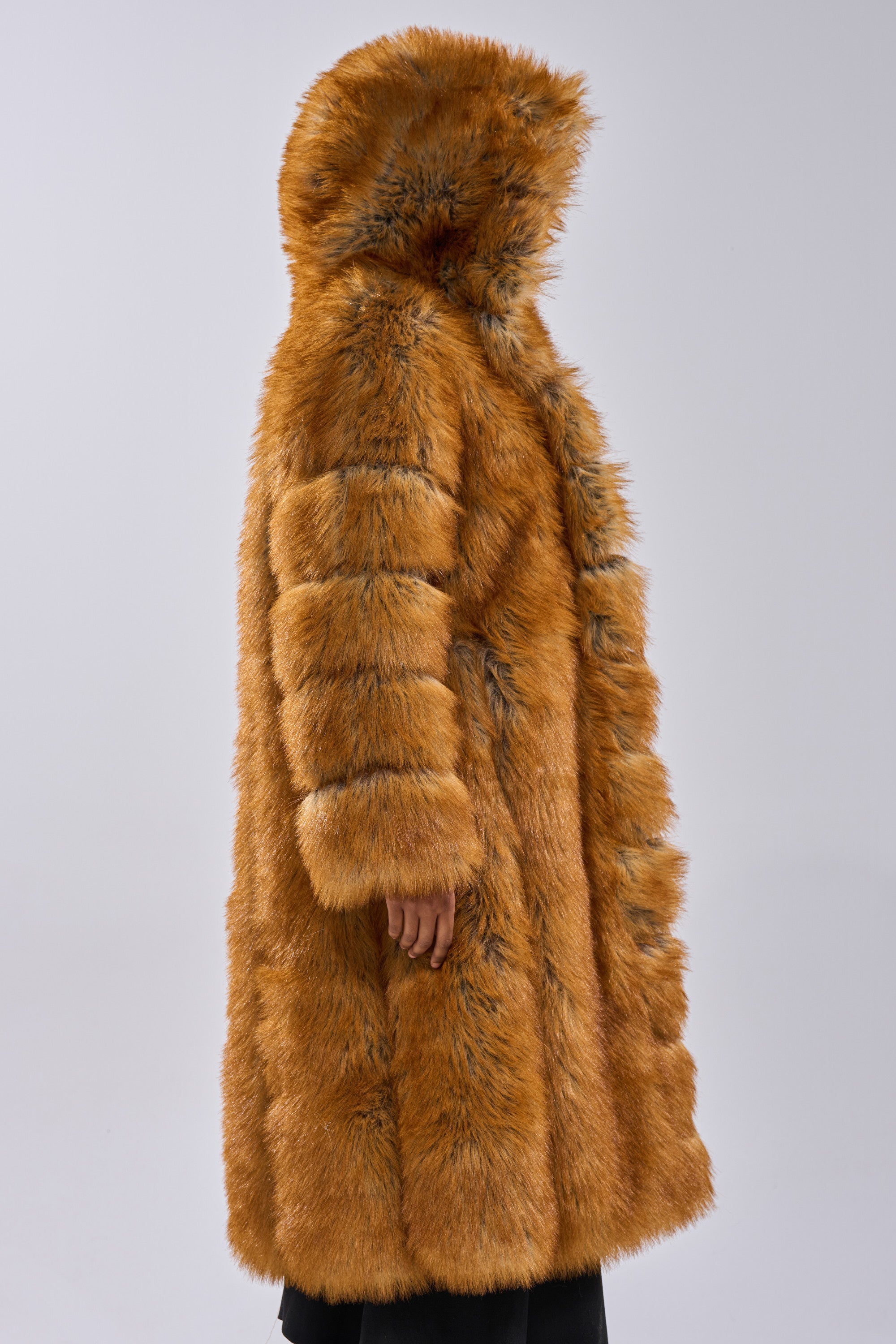A person models the OLD MONEY FAUX FUR COAT—a thick, brown, hooded faux fur outerwear—standing sideways against a plain light grey background, with only part of their face and hand visible.