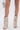 A person wears the AZALEA WANG REEVES NEW OPEN TOE PU BOOTIE IN BONE and carries a small silver wire handbag, with the photo highlighting their legs and accessories against a plain white background.