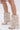 A person wears the AZALEA WANG REEVES NEW OPEN TOE PU BOOTIE IN BONE—unique beige stiletto booties resembling upside-down pants with faux pockets, buttons, textured faux leather, and a standout open toe design against a light background.