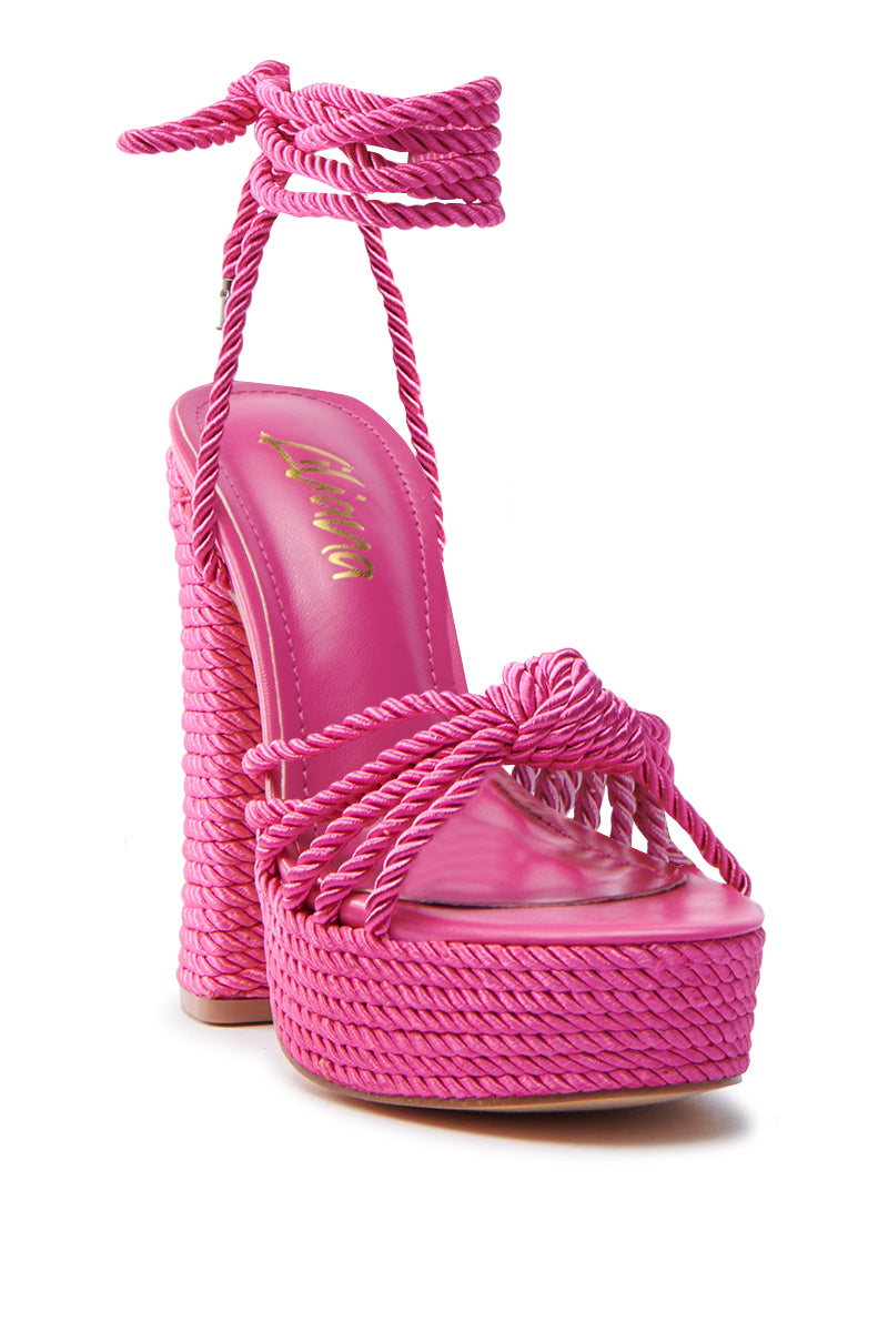 The RENEE FUCHSIA ROPE DETAIL LACE UP SANDAL is a bold fuchsia platform with braided rope straps, an ankle wrap design, and a chunky block heel. It features a faux leather insole for added comfort.