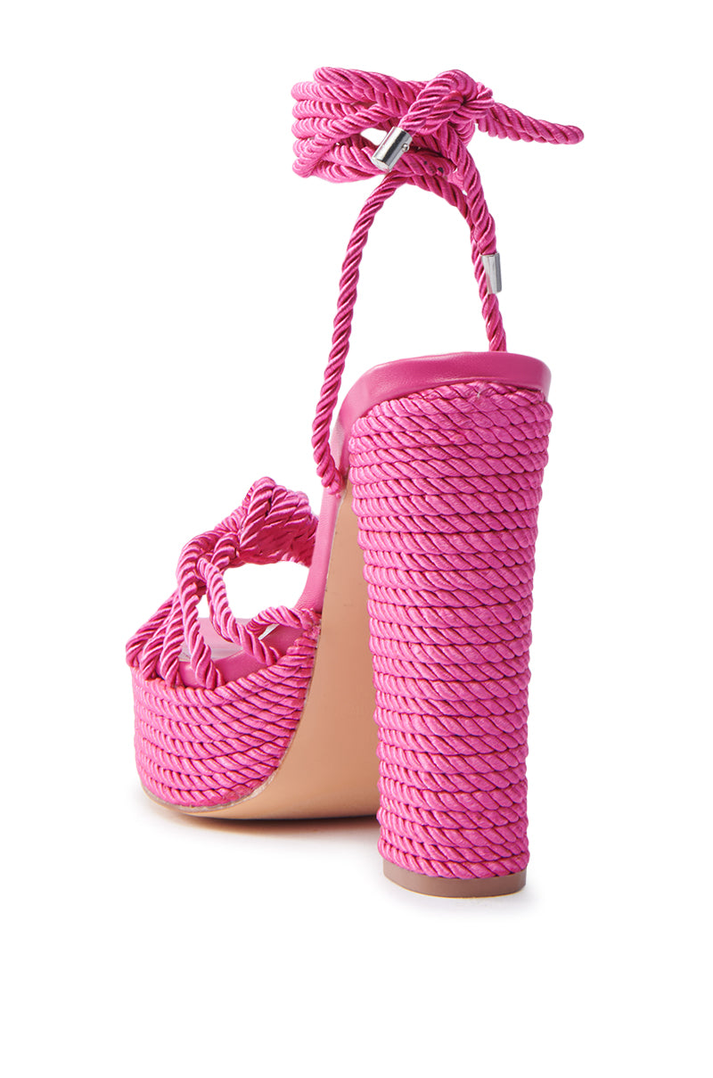 The RENEE FUCHSIA ROPE DETAIL LACE UP SANDAL features pink high heels with a woven rope design and ankle strap. It has a chunky block heel and platform with intricate rope texture, metal detail on the ankle strap, and a natural-colored sole with a comfy faux leather insole.