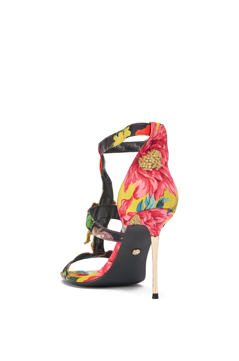 The AKIRA GOLD REPTILIAN MULTISATIN STRAP STILETTO SANDAL features a slim high heel, ankle and foot straps, and a vibrant multicolor tropical print in red, yellow, and green, shown from the back. 7