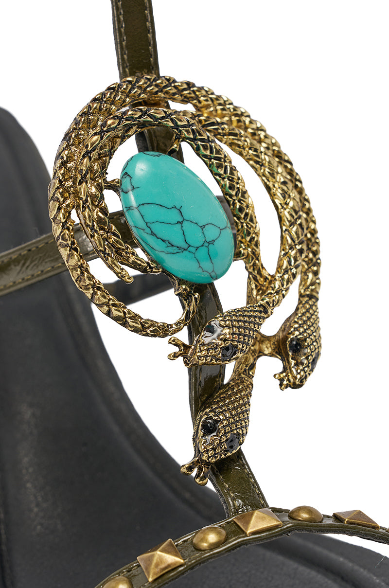 The AZALEA WANG REPUTATION OLIVE PU EMBELLISHED STILETTO SANDAL features olive faux leather, a gold-tone ornament with three intertwined snakes, a central oval turquoise stone, black gemstone eyes, gold studs, and bold statement heels. 6
