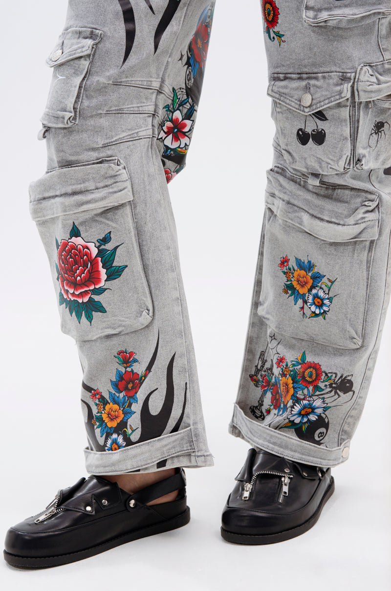 A close-up of gray cargo pants with colorful floral, cherry, and flame designs paired with the AZALEA WANG RESTER BLACK HARDWARE EMBELLISHED MULE featuring metallic zipper detailing and metal ring accents.