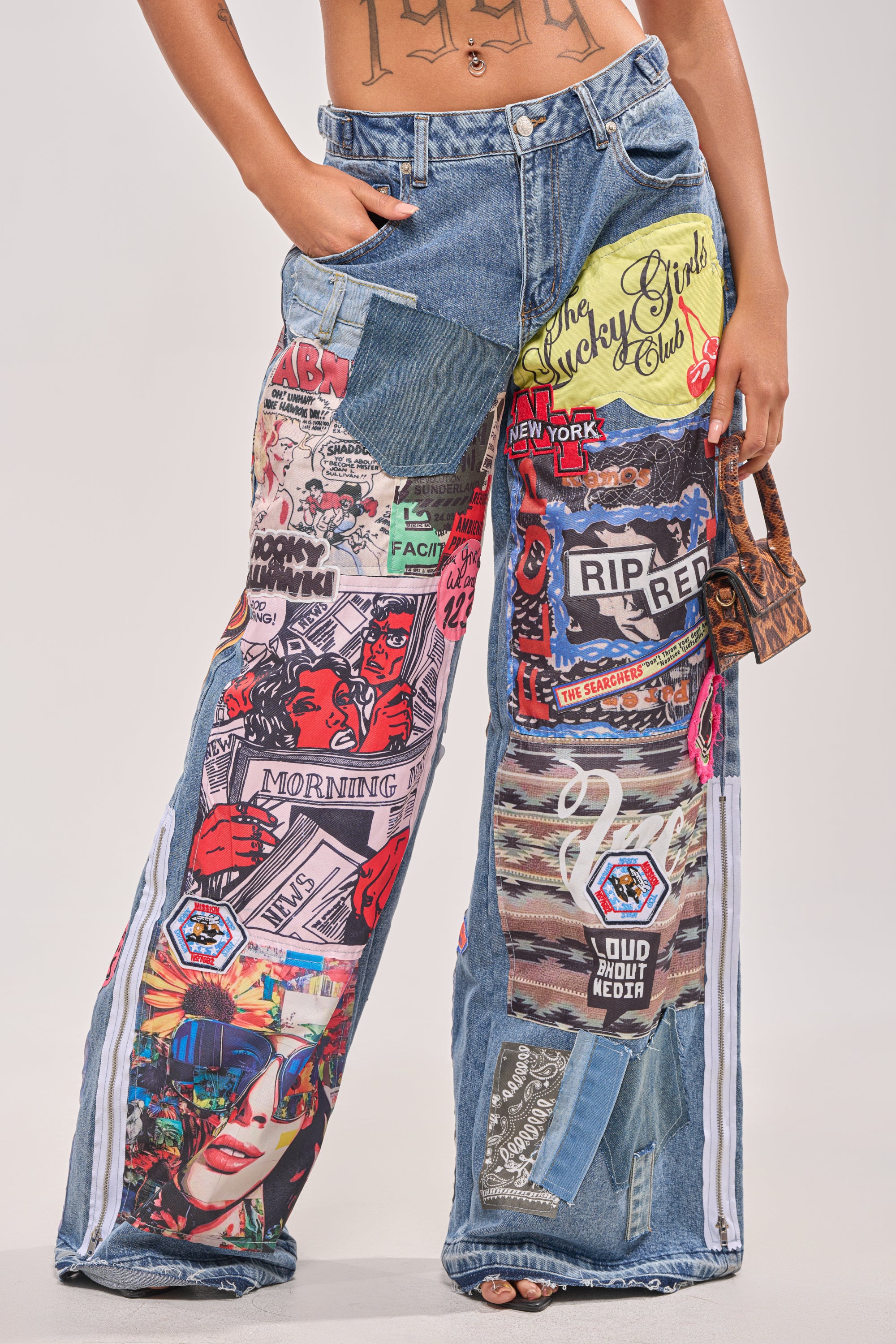A person wearing SO SICK SO COOL VERY OVERSIZED DENIM—streetwear-inspired ultra-wide leg jeans with colorful comic book-style patches, pop art graphics, and text—holds a small brown handbag; torso and head not visible. 0