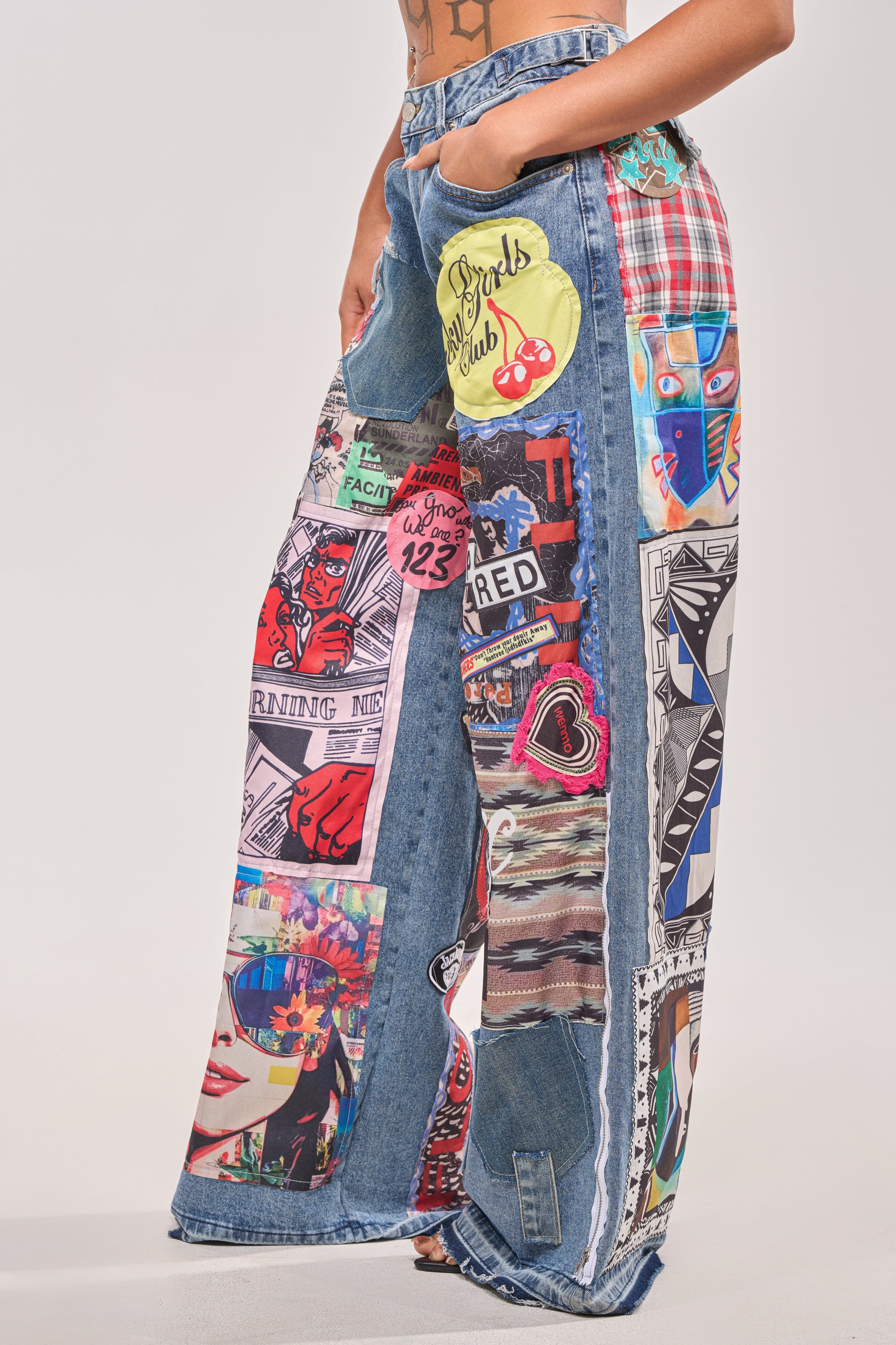A person wears SO SICK SO COOL VERY OVERSIZED DENIM jeans featuring bold graphic patches and comic-style illustrations; only the waist-down is visible against a plain background. 3