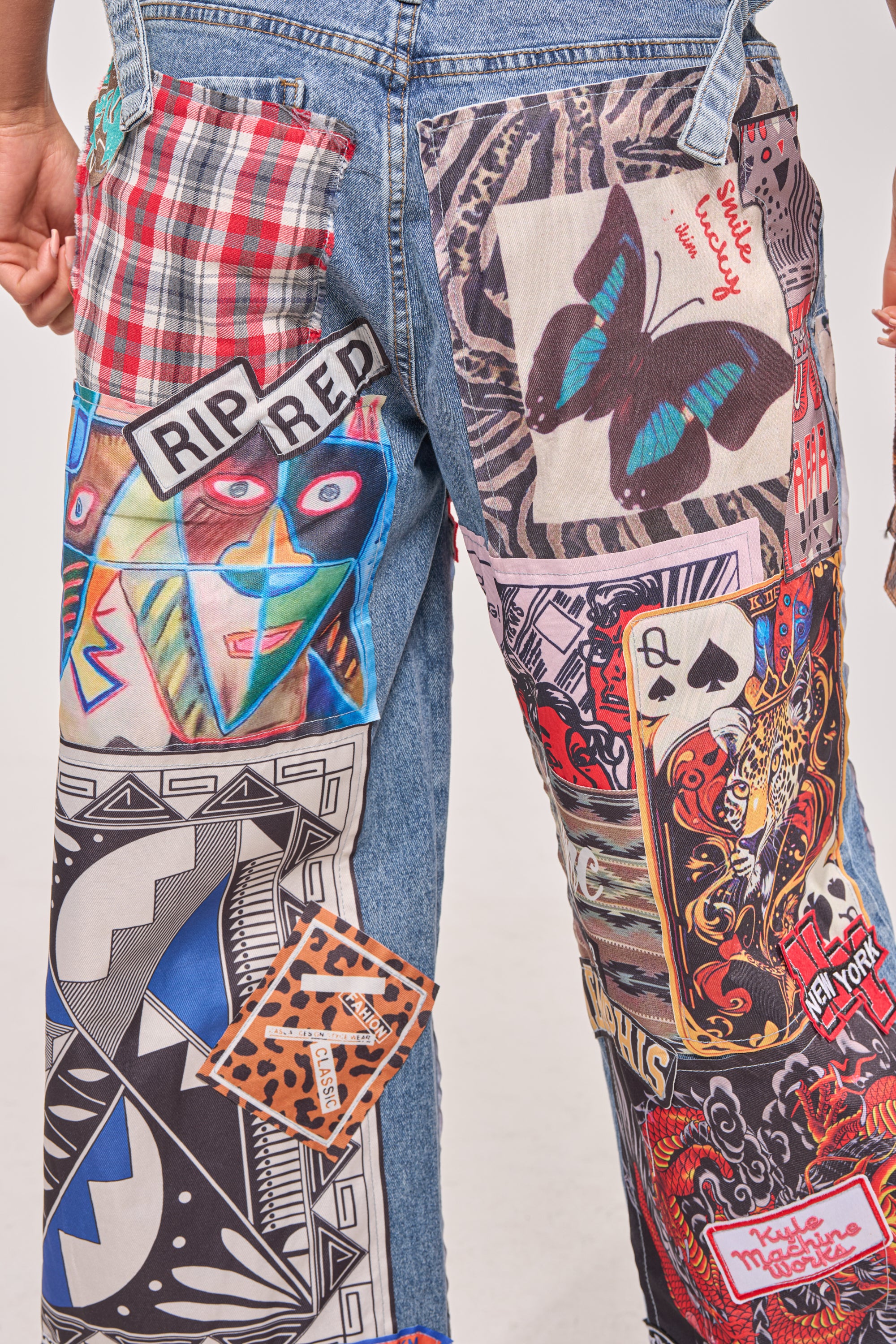 Close-up of SO SICK SO COOL VERY OVERSIZED DENIM streetwear jeans featuring colorful patches—a blue butterfly, face, playing cards, plaid fabric, bold geometric patterns, and text reading "RIP RED" and "New York" on a white background. 8