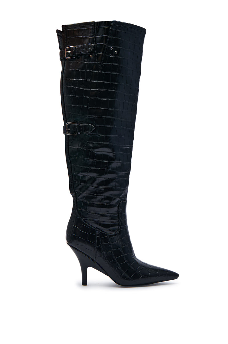 The AZALEA WANG RHODES BLACK CROC WEDGE BOOT is a black knee-high boot made from faux crocodile leather, featuring a pointed toe, wedge stiletto heel, and two adjustable buckles on the side.