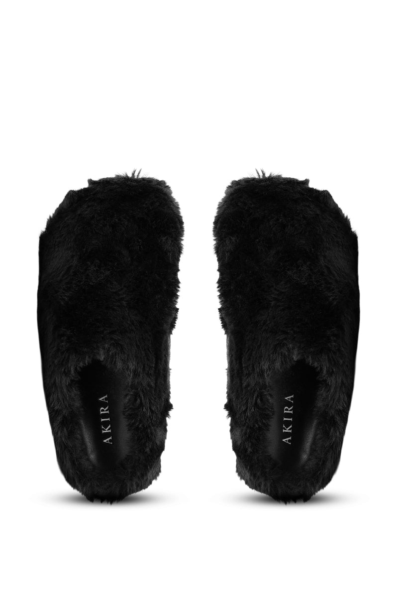 A pair of AKIRA RHYS BLACK FUZZY FLAT shoes with thick black faux fur, viewed from above. The fleece-lined insoles display "AKIRA" in white lettering.
