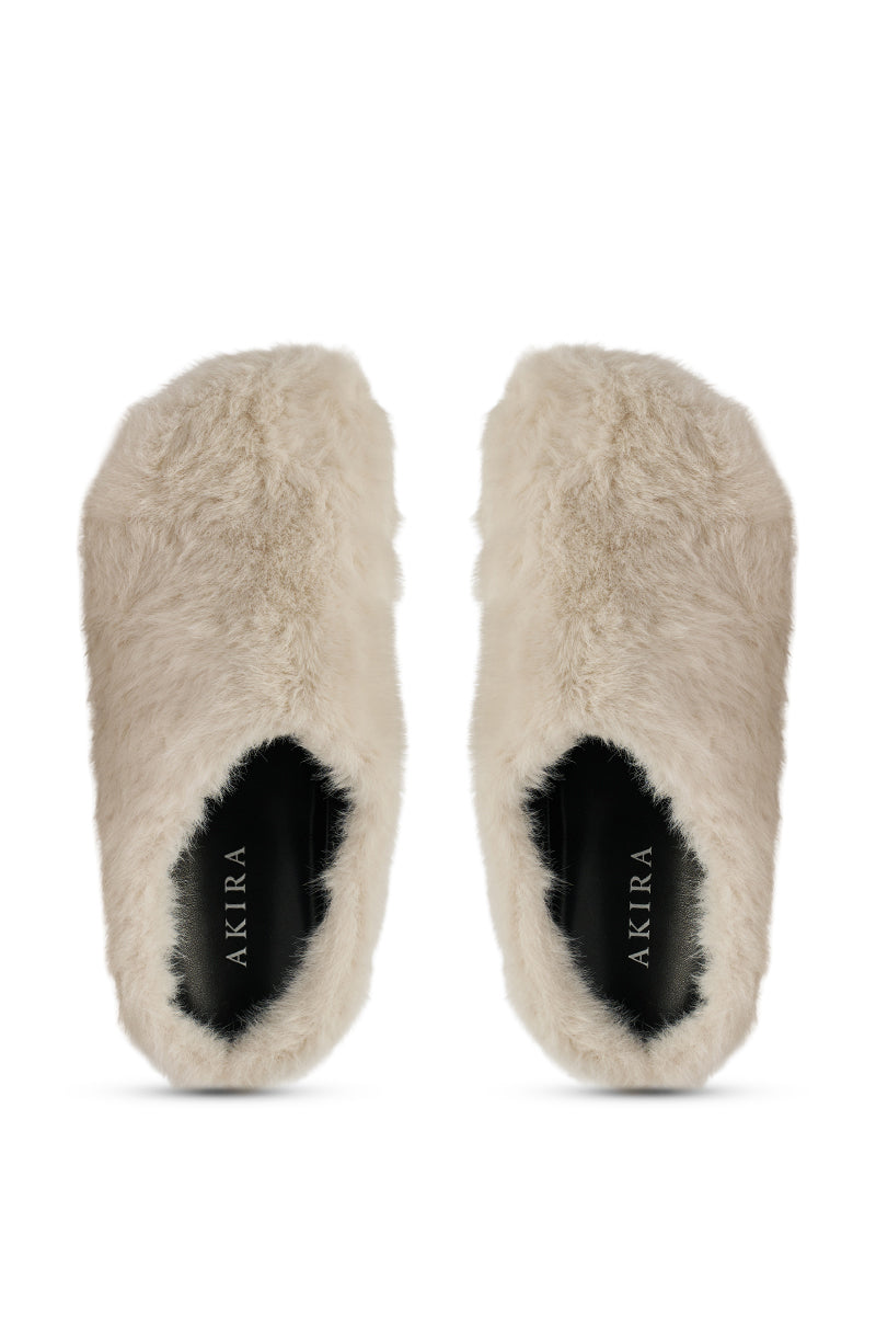 The AKIRA RHYS IVORY FUZZY FLAT is a pair of beige, fleece-lined, fluffy slip-on slippers with almond toes and black insoles labeled "AKIRA," shown from above on a white background.