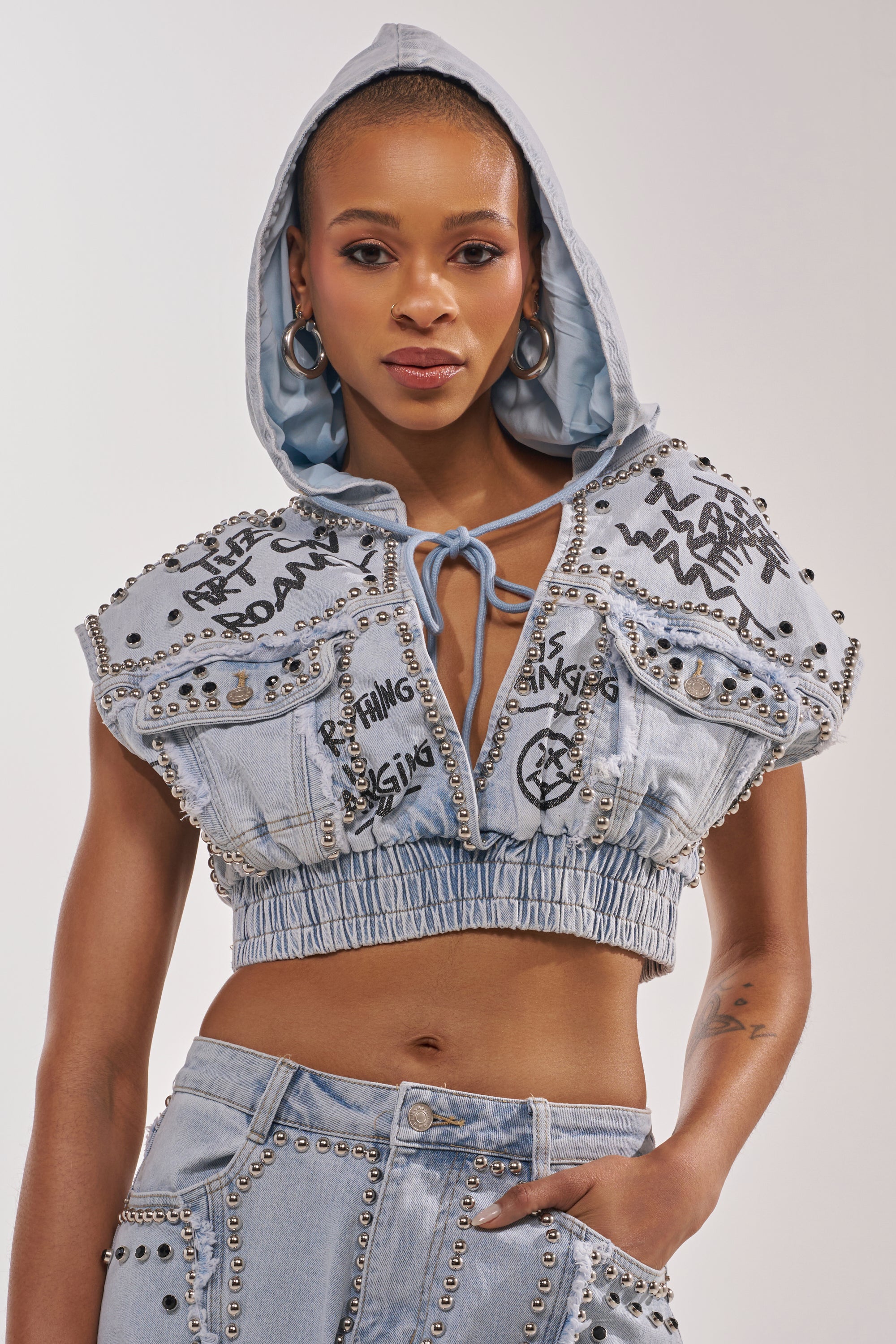Wearing the GET INTO THE RHYTHM CROP HOODIE with high-waisted pants, metal studs, and graffiti graphics, she completes her street-chic look with hoop earrings and confidence. 0
