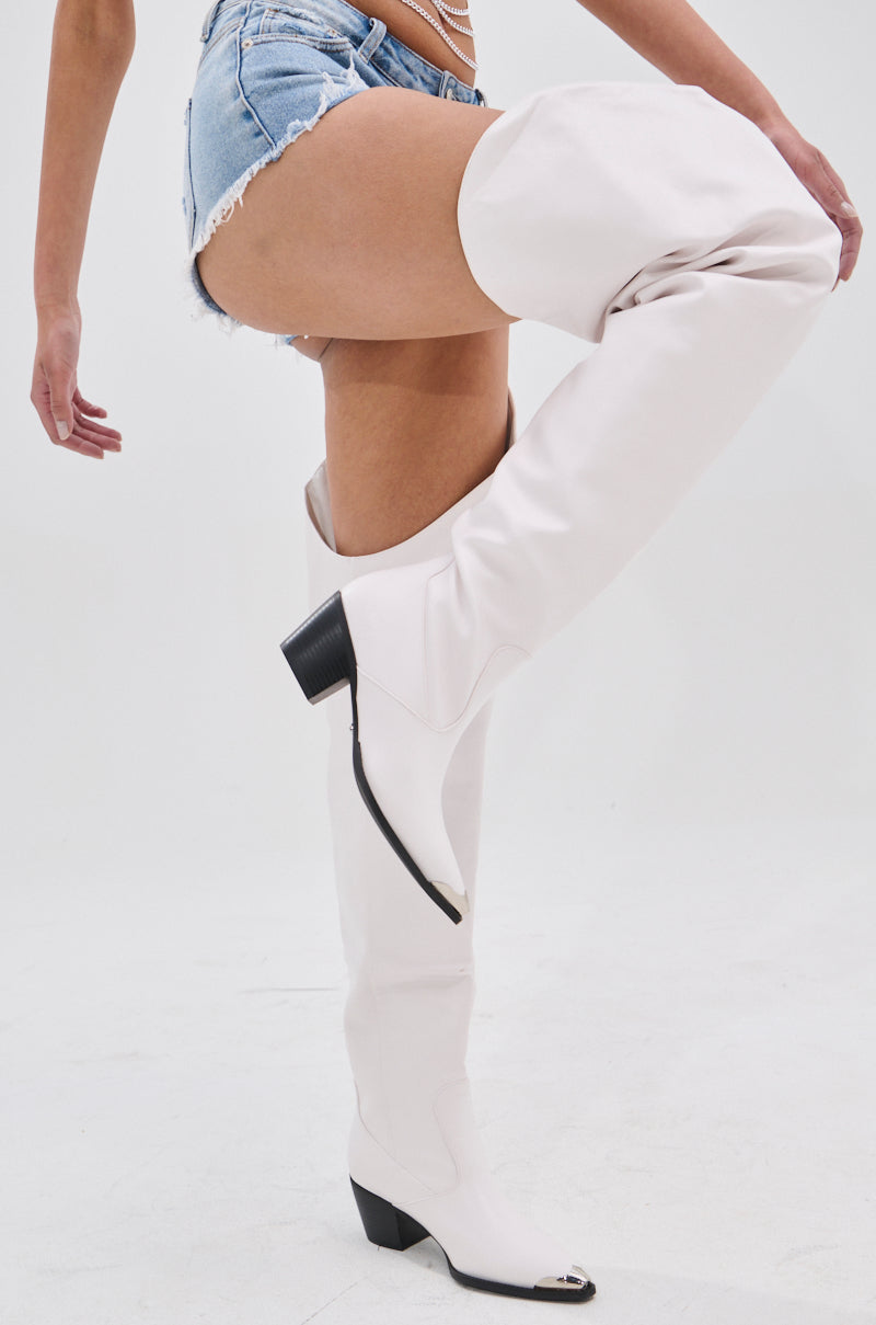 Wearing chic AZALEA WANG RIA Over the Thigh Western Boots in white with black heels and distressed denim shorts, a person stands against a white background, highlighting an edgy yet minimalist look.
