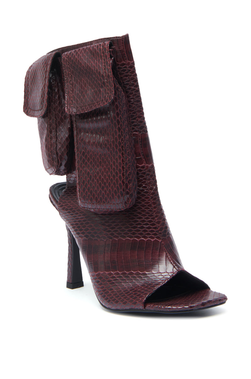 The AZALEA WANG RIDWAN BURGUNDY SNAKE OPEN TOE BOOTIE is a high-heeled, square peep toe shoe in shiny snakeskin-inspired burgundy faux leather with two bold flap pockets at the ankle.
