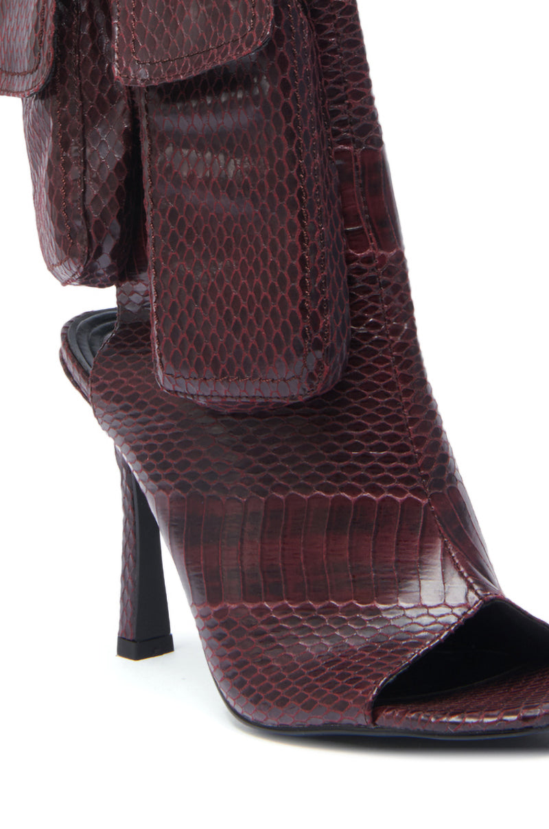 The AZALEA WANG RIDWAN BURGUNDY SNAKE OPEN TOE BOOTIE features glossy faux leather snakeskin, a square peep toe, and a bold pocket detail at the ankle.