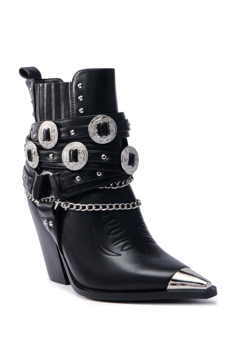 The AZALEA WANG RIGGINS BLACK SILVER HARDWARE EMBELLISHED WESTERN BOOTIE features vegan leather, decorative silver buckles, studs, chains, a pointed toe with a metal tip, and embossed detailing for an edgy look.