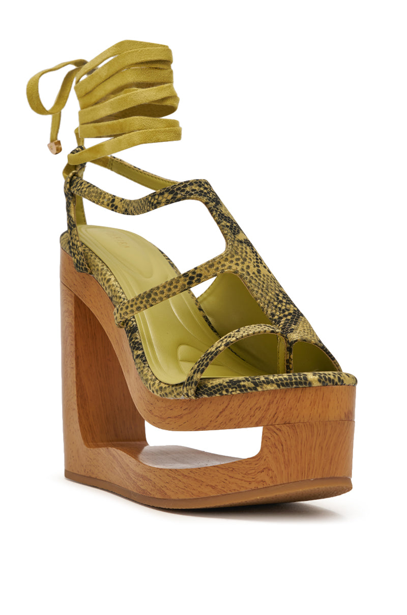The AKIRA GOLD RIN GREENSNAKE NOVELTY LACE UP WEDGE SANDAL features a yellow-green snakeskin print, open toe, sparkly lace-up ankle straps, and a unique wooden platform heel with cut-out detailing. 6
