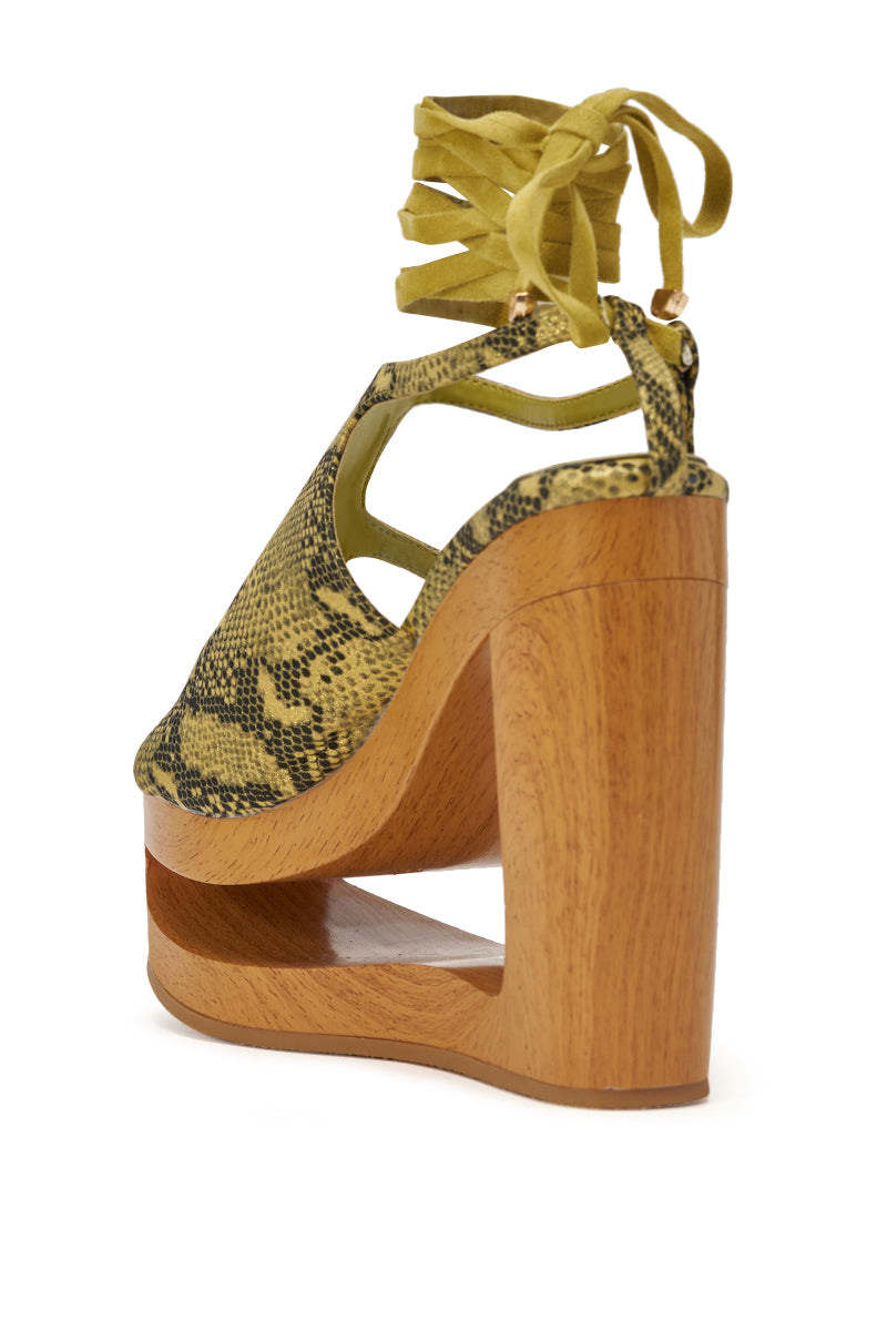 Step out in standout style with the AKIRA GOLD RIN GREENSNAKE NOVELTY LACE UP WEDGE SANDAL, featuring a bold snake print, wood platform, high heel, open back, cutout heel design, and ankle wrap laces tied in a bow. 7