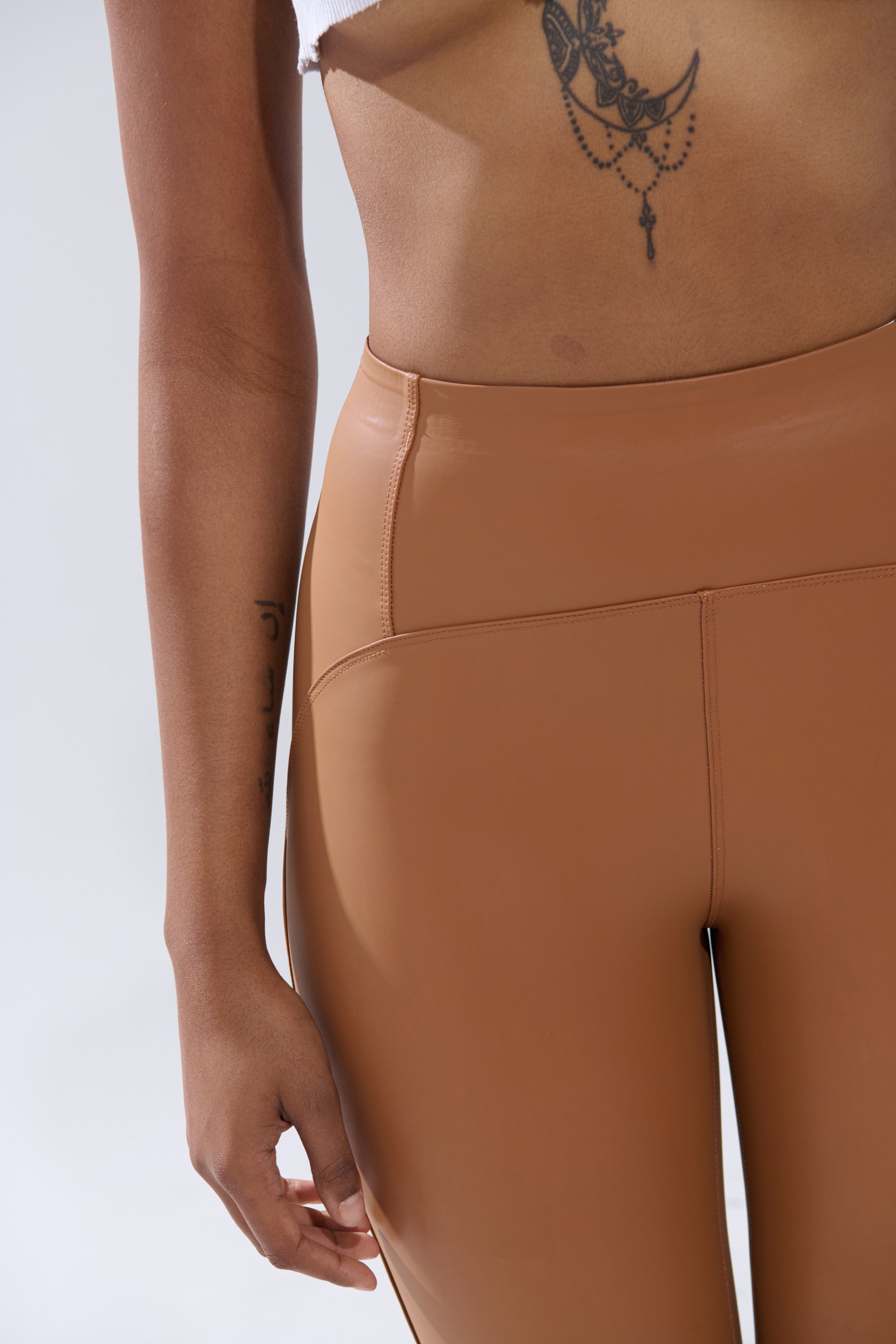 Wearing the RIO HIGH RISE LEGGING WITH 4 WAY STRETCH IN BROWN and a cropped white top, this look highlights tattoos on the forearm and ribcage—perfect for showcasing these flexible lounge essentials.