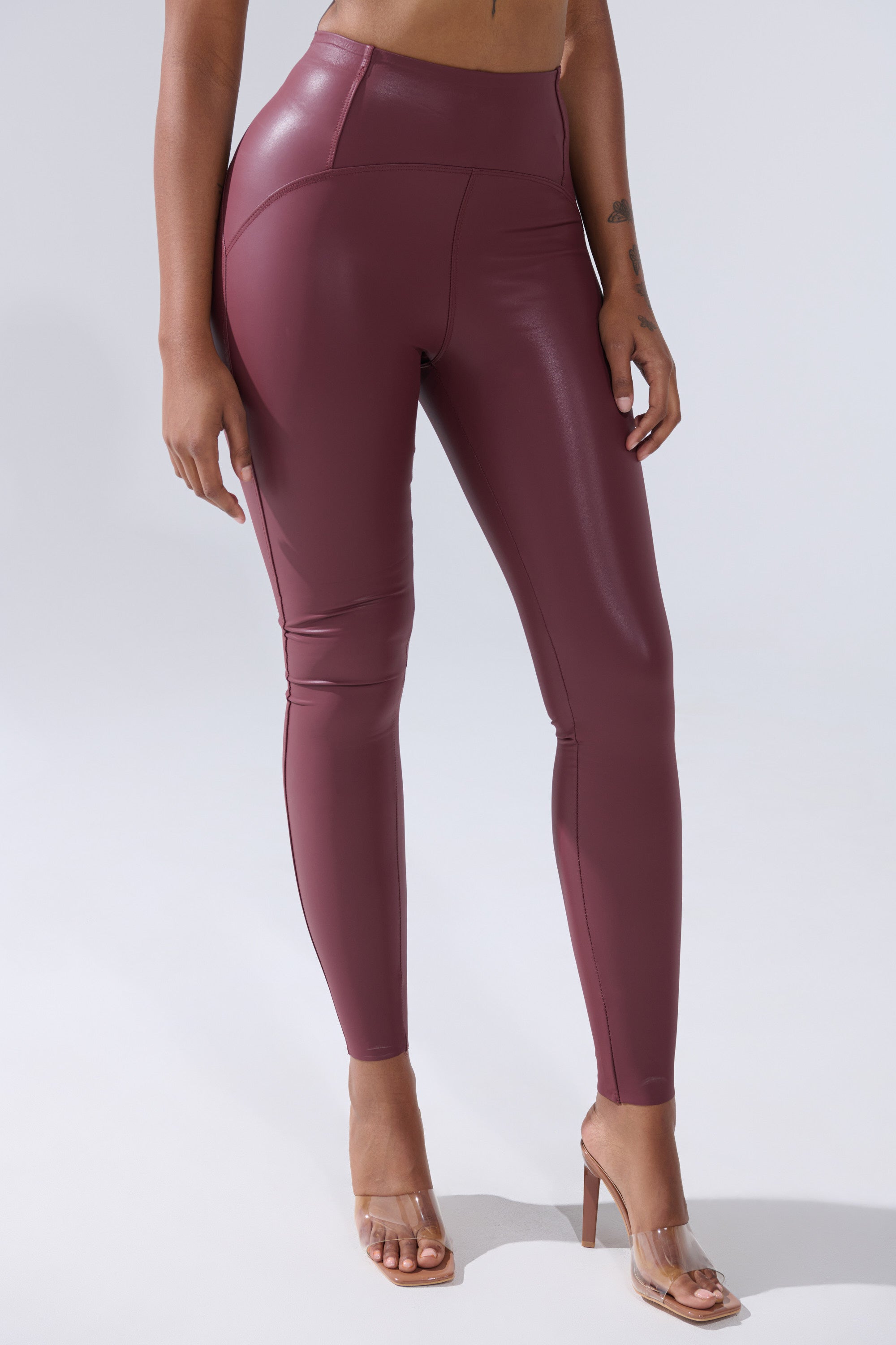 Wearing the RIO HIGH RISE LEGGING WITH 4 WAY STRETCH IN OXBLOOD and clear heeled sandals, a person stands against a plain light background, visible from shoulders down.