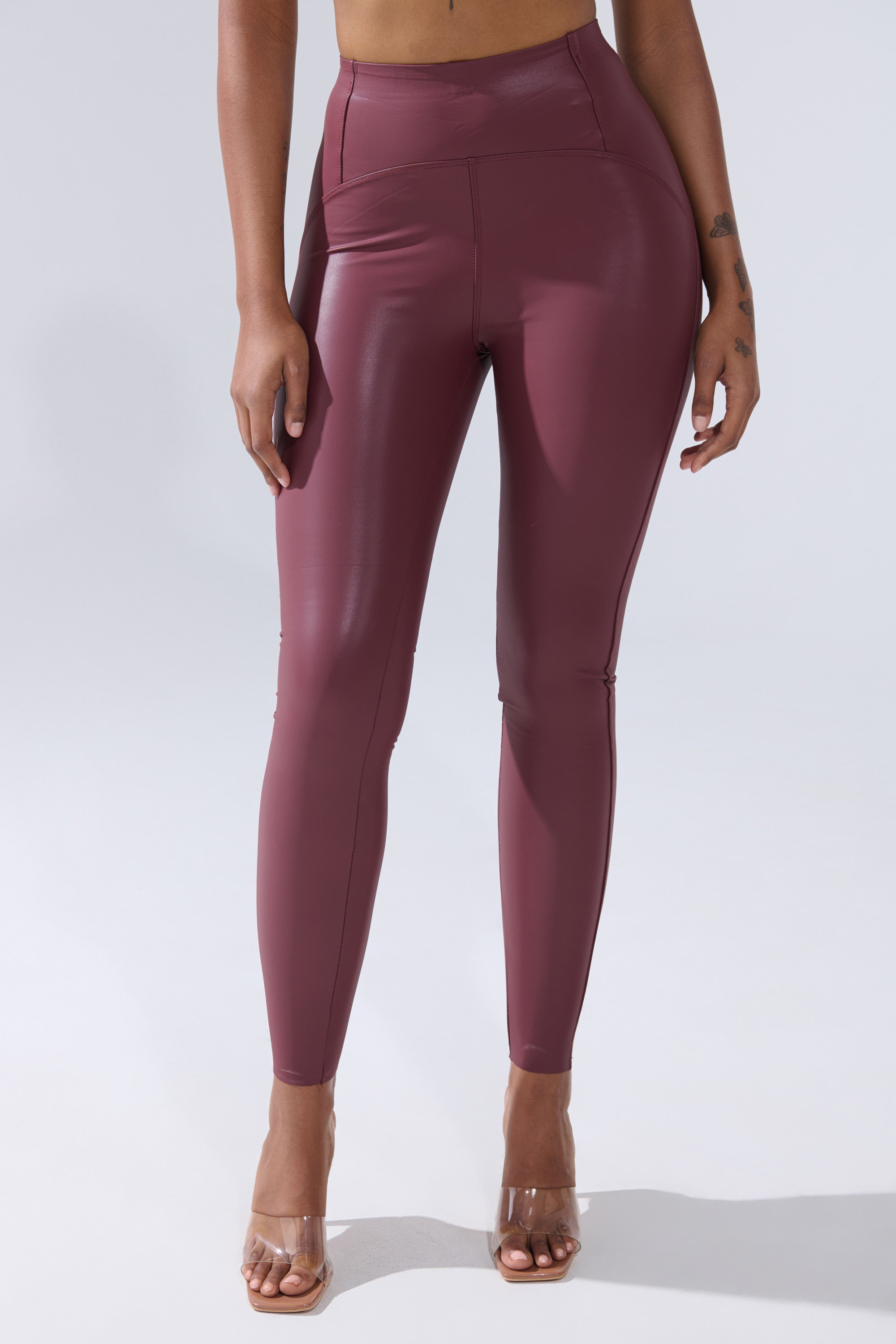 A person wears RIO HIGH RISE LEGGING WITH 4 WAY STRETCH IN OXBLOOD and clear heels, shown from the waist down against a plain light background.