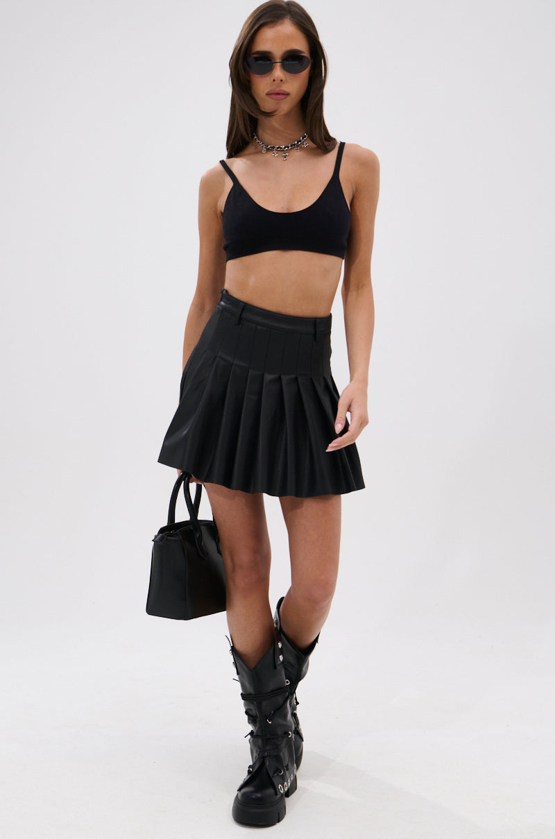 A woman wearing sunglasses, a black crop top, chunky black boots, a choker, and holding a small black handbag showcases the RIO Pleated Faux Leather Mini Skirt with 4 Way Stretch against a plain white background.