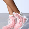 A person wearing AZALEA WANG RIORDAN PINK FUR HIGHTOP SNEAKERS, featuring vibrant pink faux fur and white laces, perfectly pairs these stylish sneakers with knee-length frayed denim shorts against a plain background.