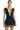 A person stands facing forward, wearing a navy blue ALWAYS LUCKY RIBBED COLLARED BODYSUIT by AKIRA. The short-sleeve knit bodysuit features a yellow collar, yellow stripes on the sleeves, and an open front with yellow buttons. They are also wearing a pleated navy blue skirt with yellow stripes near the hem.