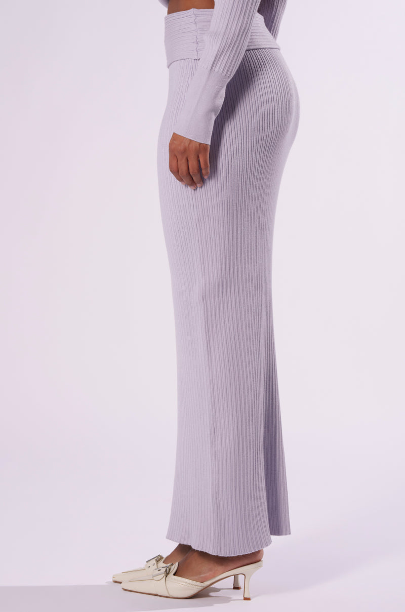 Side view of a person wearing the CAN'T LOSE SWEATER KNIT MIDI SKIRT in light purple, paired with a matching long-sleeved top. The bodycon fit ensemble is complemented by white low-heeled shoes with decorative buckles. The background is plain white. 2