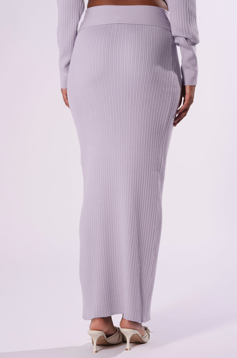 A person wearing a fitted, light gray CAN'T LOSE SWEATER KNIT MIDI SKIRT by AKIRA Label that extends to the ankles. This knit midi skirt is paired with light-colored, pointed-toe heeled shoes. The image captures a rear view of the ensemble, highlighting the texture and bodycon fit of the skirt. 3