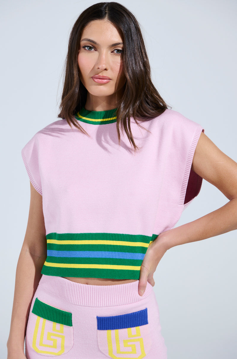 A person is rocking a sporty-chic look with a light pink sleeveless top featuring green and yellow stripe accents and long dark hair. They're pairing it with a matching pink skirt adorned with vibrant pocket designs, perfectly embodying the AKIRA Label style and the LOVE WINS SWEATER vibe.