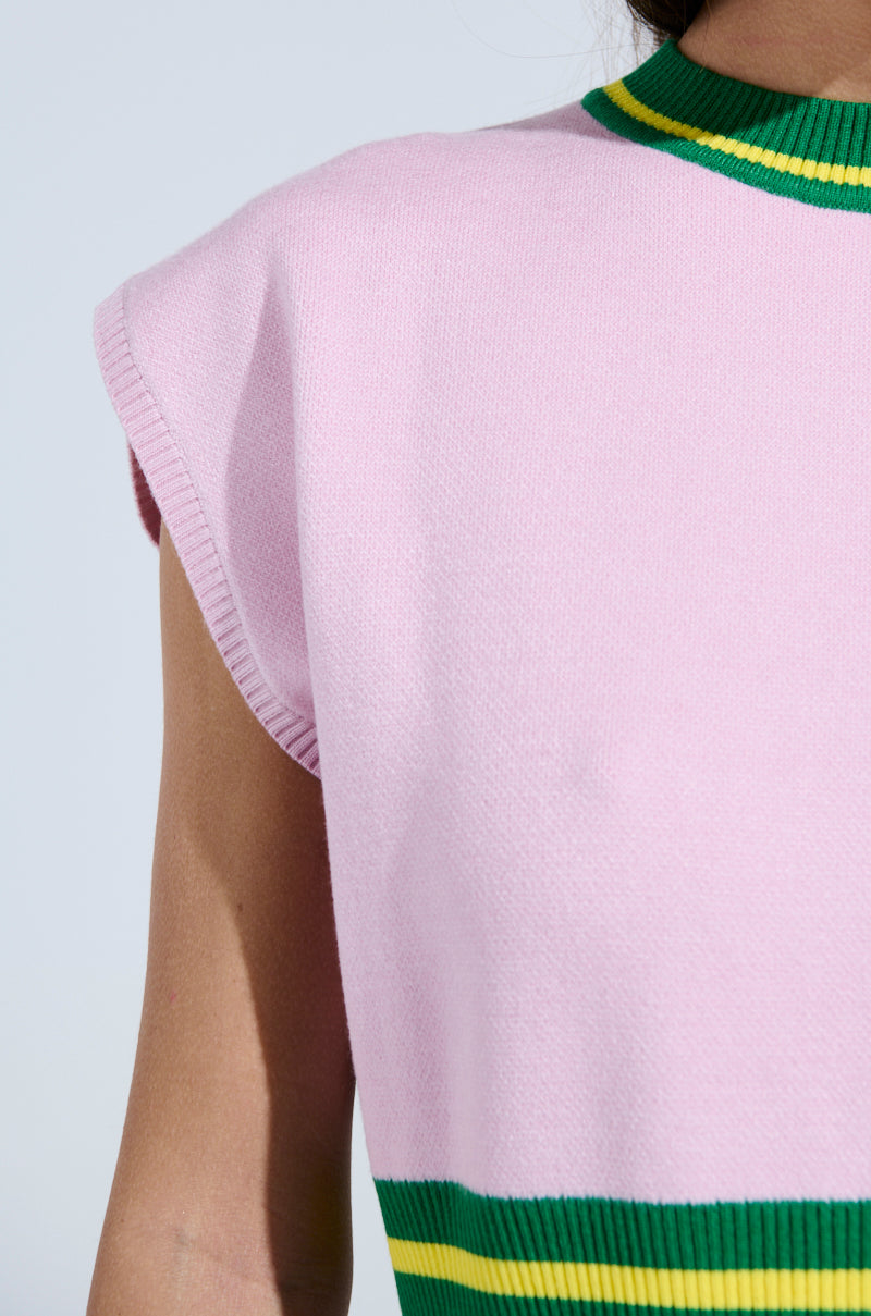 A person wears the LOVE WINS SWEATER, a sleeveless top with a pink body, green collar, and yellow-green stripes below the chest. This sporty-chic ensemble highlights the upper body against a neutral backdrop for effortless style.