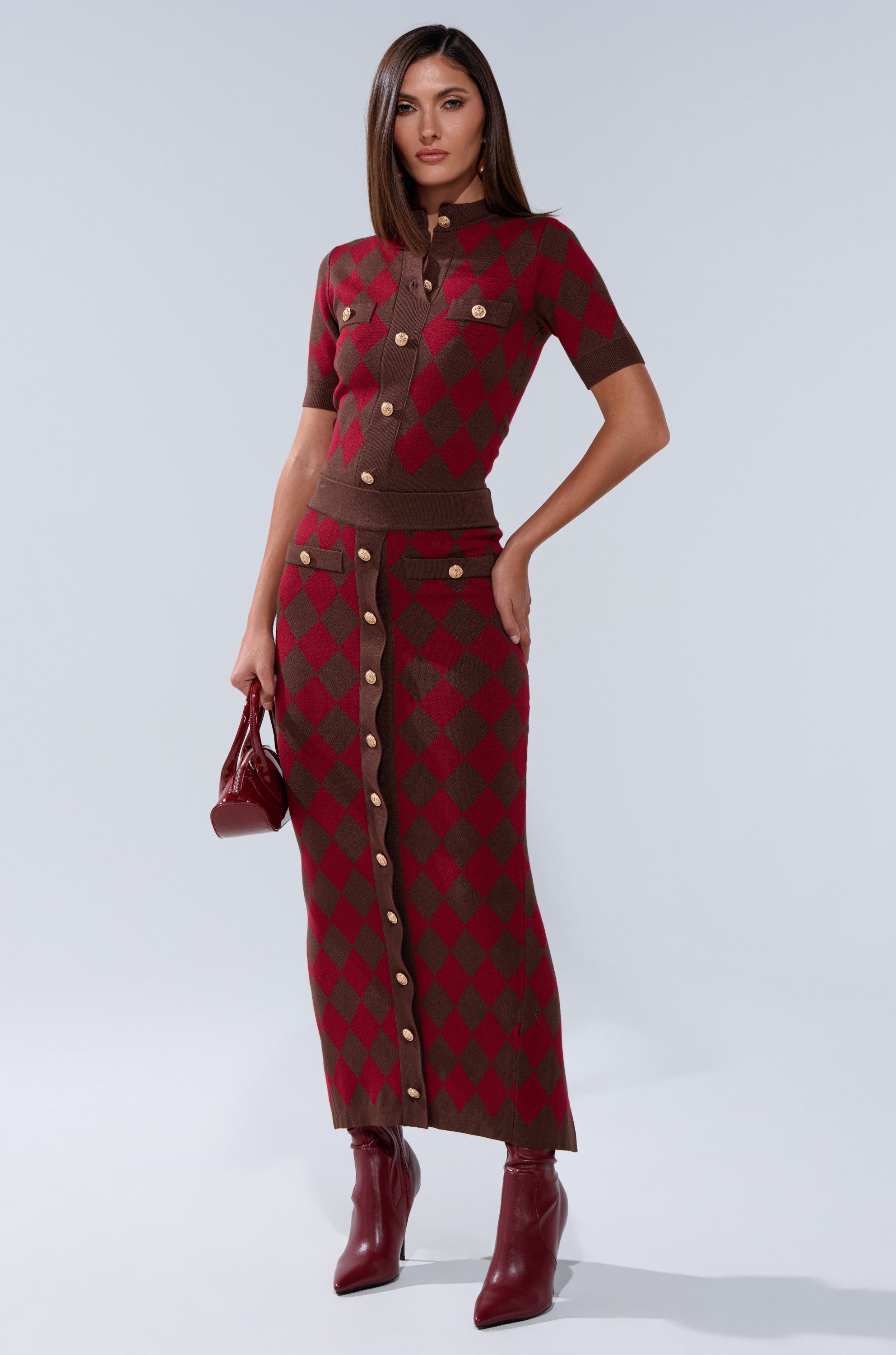 A woman stands against a plain light background, wearing THE BEST PART OF THIS ABSTRACT MAXI SKIRT with a knit top, ankle boots, and holding a small handbag.