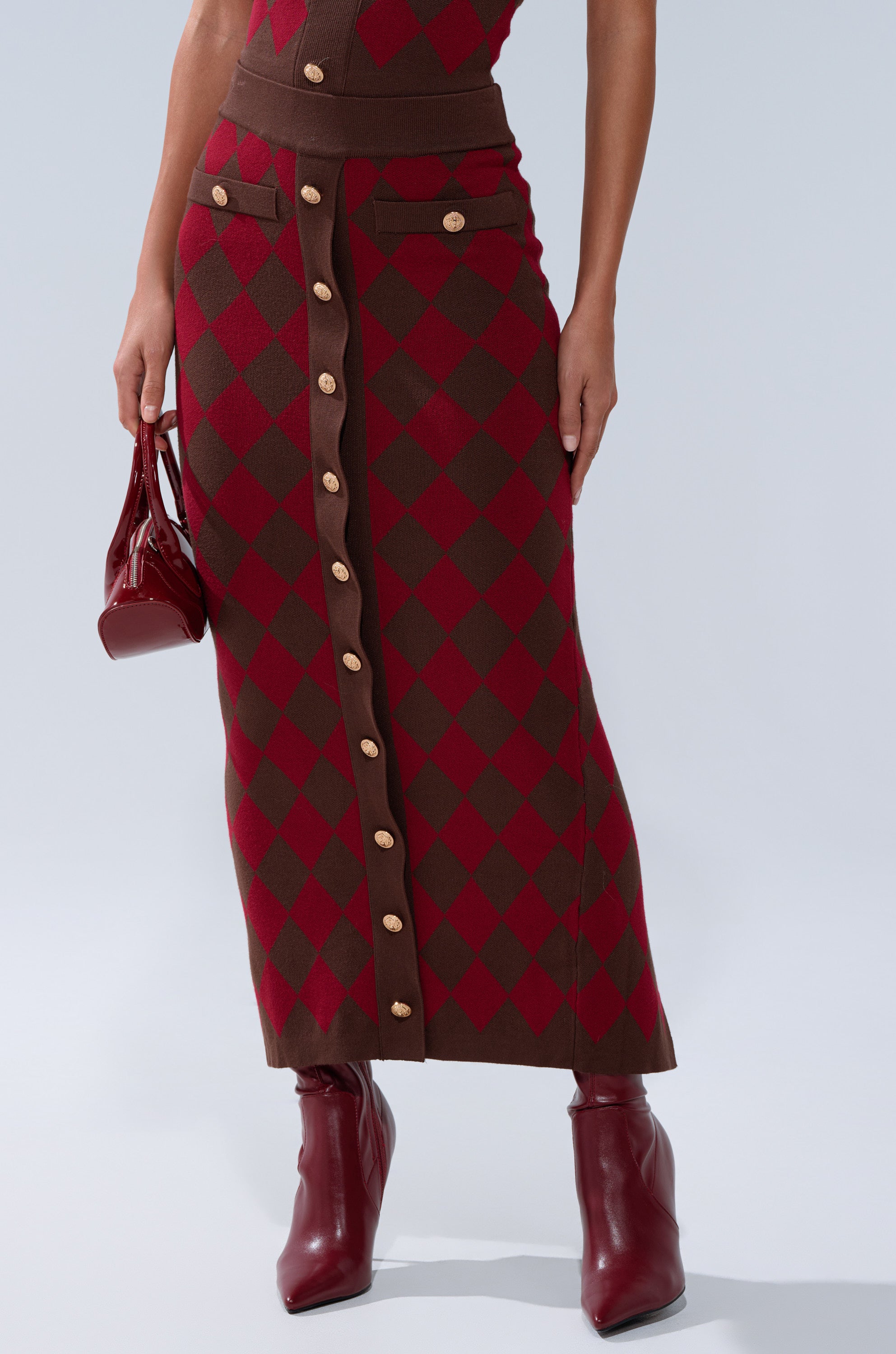 Someone wearing THE BEST PART OF THIS ABSTRACT MAXI SKIRT paired with red ankle boots and holding a small shiny red handbag.