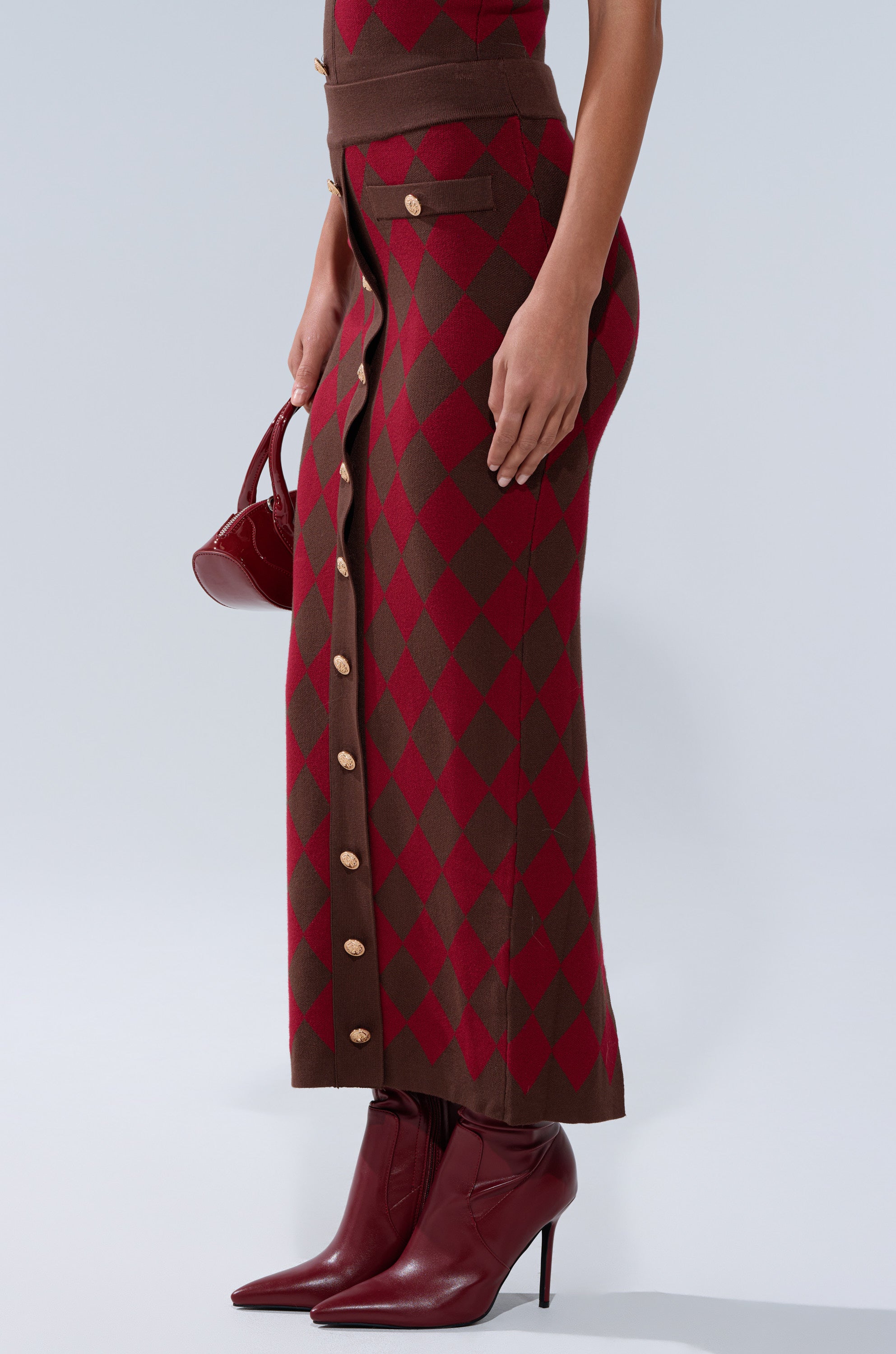 A person wears THE BEST PART OF THIS ABSTRACT MAXI SKIRT, styled with matching pointed high-heeled boots and a small red handbag. Only the lower body is visible.