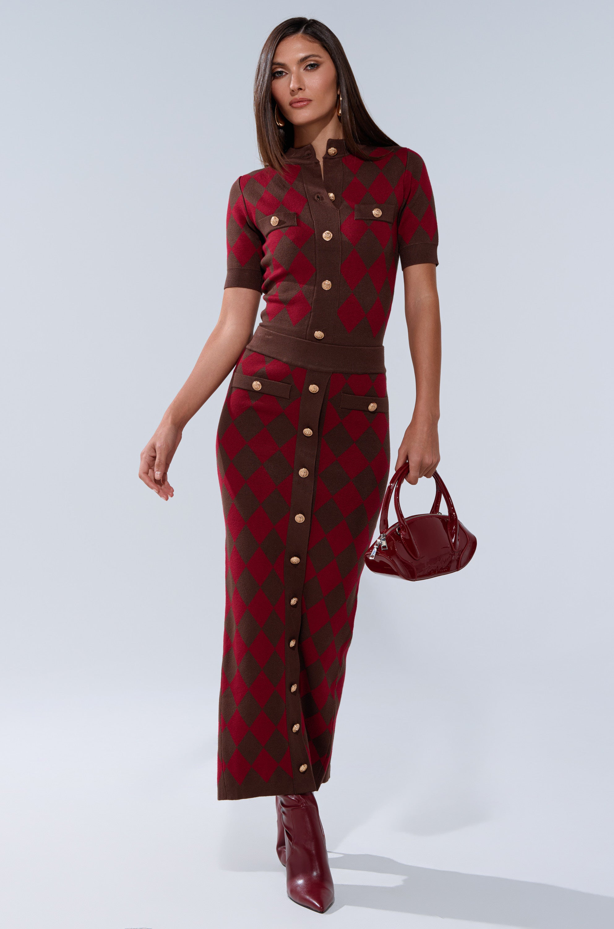 A woman poses confidently in THE BEST PART OF THIS ABSTRACT MAXI SKIRT, styled with gold buttons, matching ankle boots, and a small burgundy handbag against a plain light background.