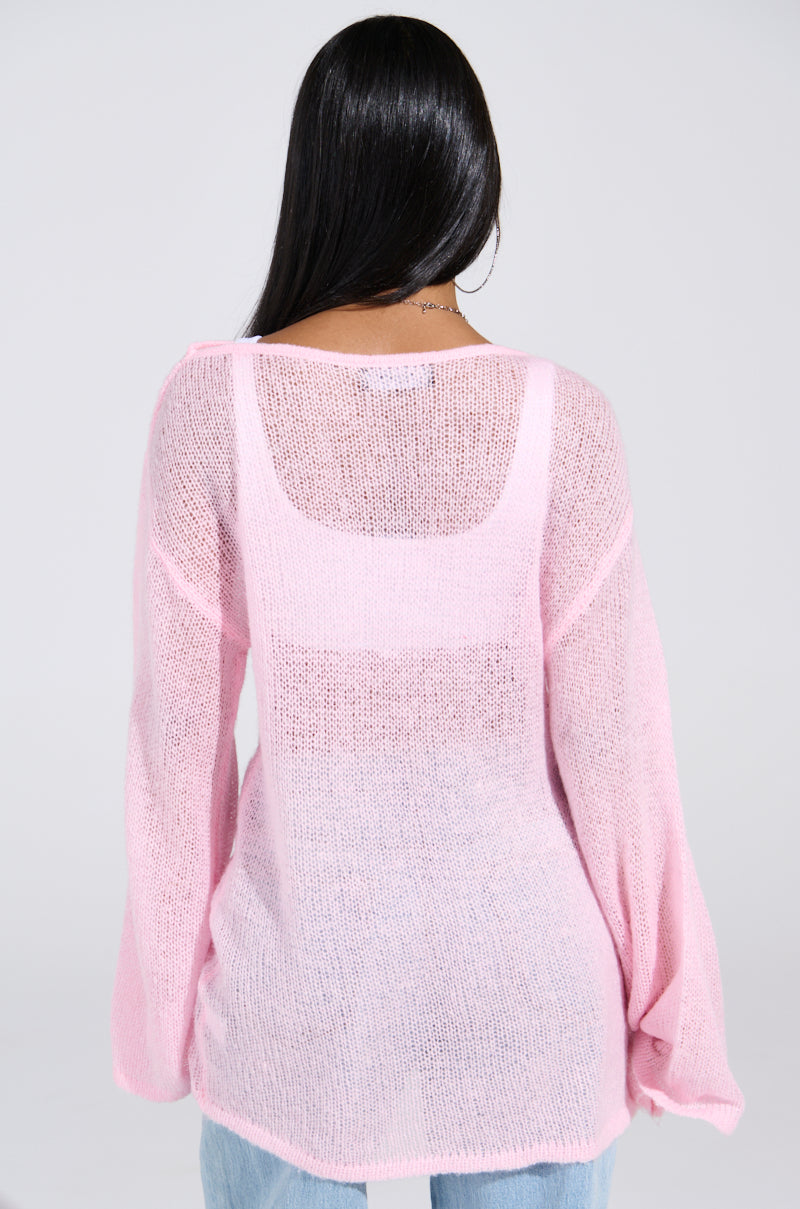 A person with long dark hair, viewed from behind, is wearing the BE READY IN 5 SWEATER DRESS in sheer pink, styled with an oversized fit over a tank top. They pair it with light blue jeans against a simple gray background.