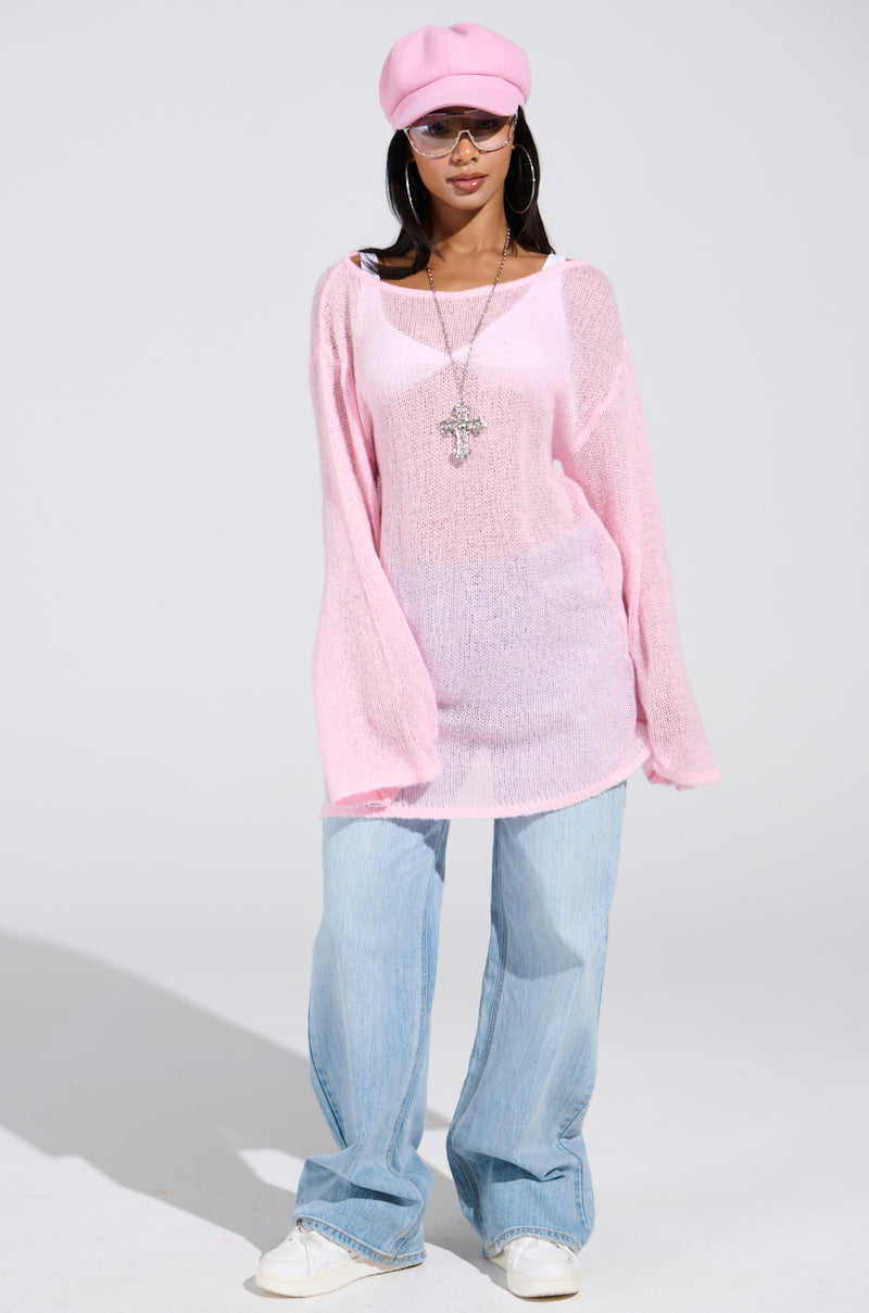 A person wearing a BE READY IN 5 SWEATER DRESS in sheer pink over a white top, paired with light blue wide-legged jeans, white sneakers, and a pink beret. They accessorize with large hoop earrings, sunglasses, and a long necklace featuring a large cross pendant.