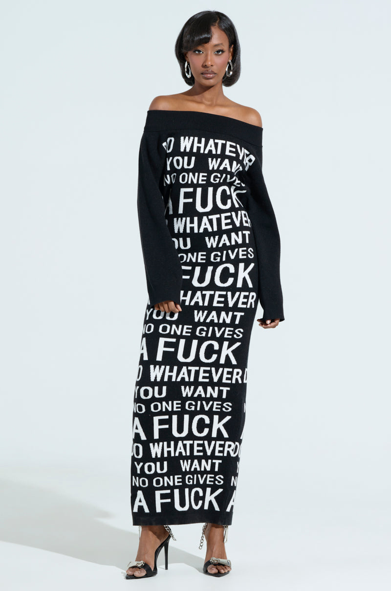 A woman in the WHATEVER YOU WANT KNIT MAXI DRESS, featuring an off-the-shoulder, open-back design with bold white text and explicit language. Styled elegantly with high heels and hoop earrings against a light background.