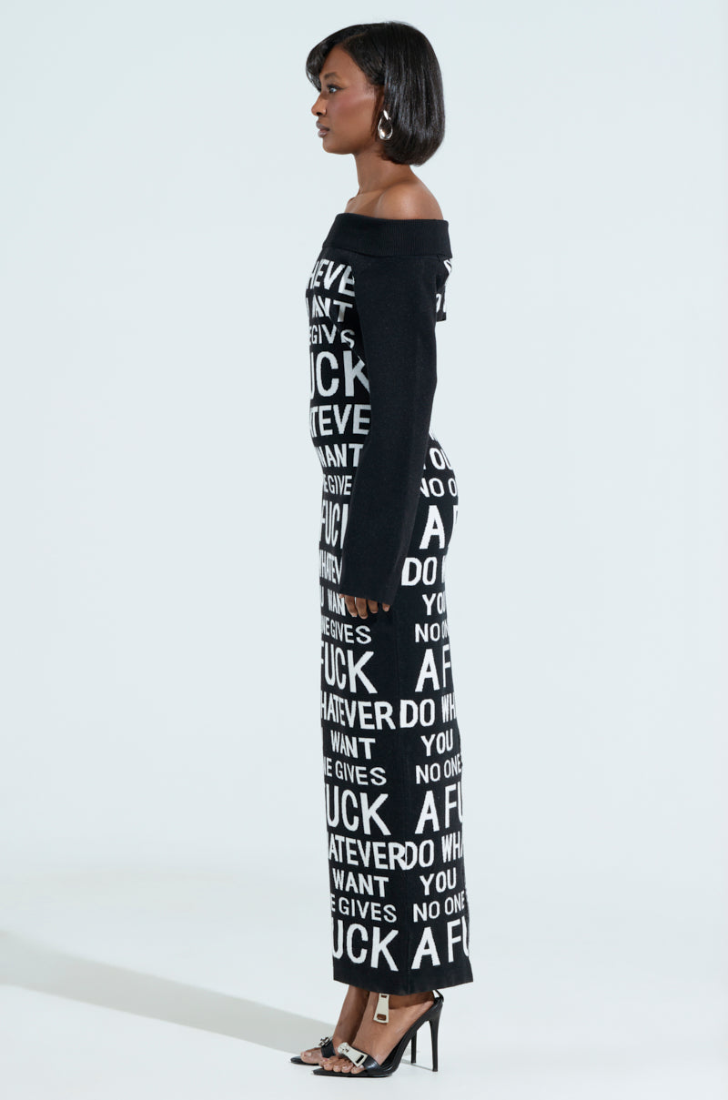 A person in profile wears the WHATEVER YOU WANT KNIT MAXI DRESS, a curve-hugging, long off-shoulder black dress with bold white phrases like "A F***" and "WHATEVER." Paired with black high-heeled sandals, the outfit radiates confidence.
