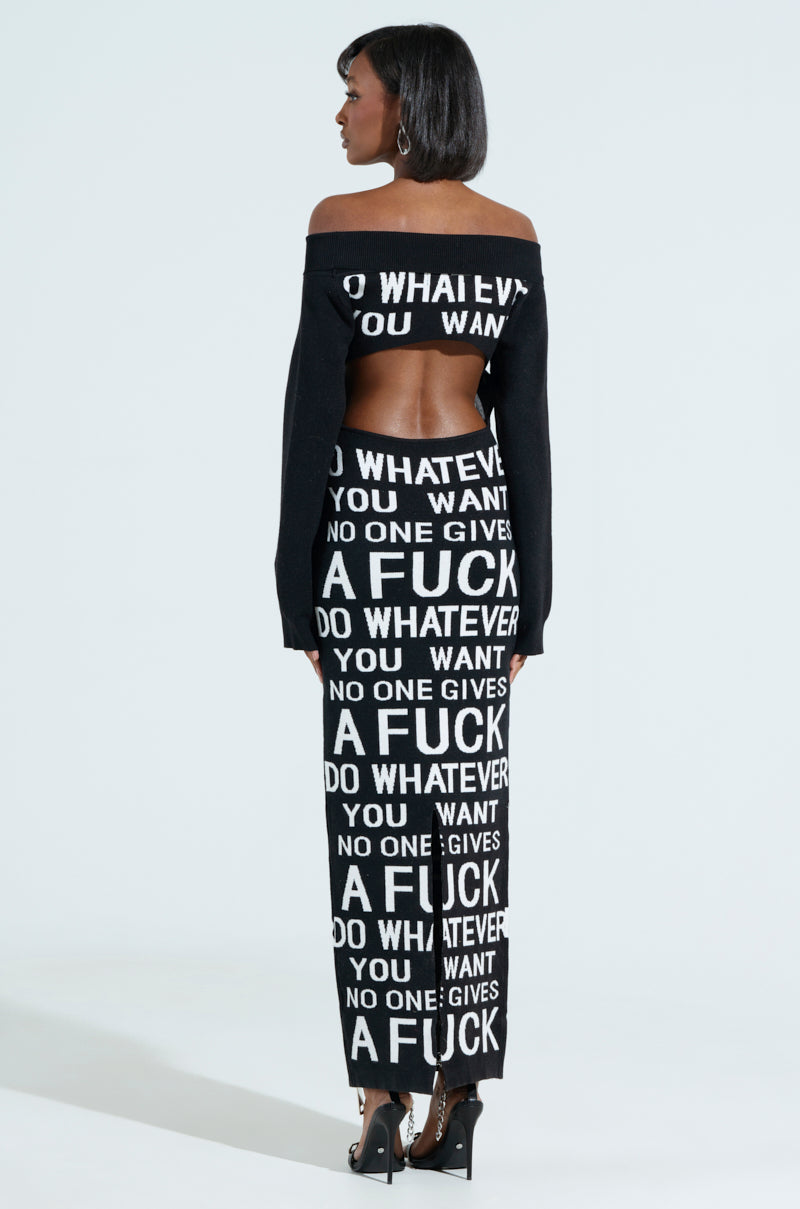 Facing away, a person dons the curve-hugging WHATEVER YOU WANT KNIT MAXI DRESS. The off-shoulder black outfit features bold white text saying "DO WHATEVER YOU WANT NO ONE GIVES A FUCK," revealing part of the back against a light gray backdrop.