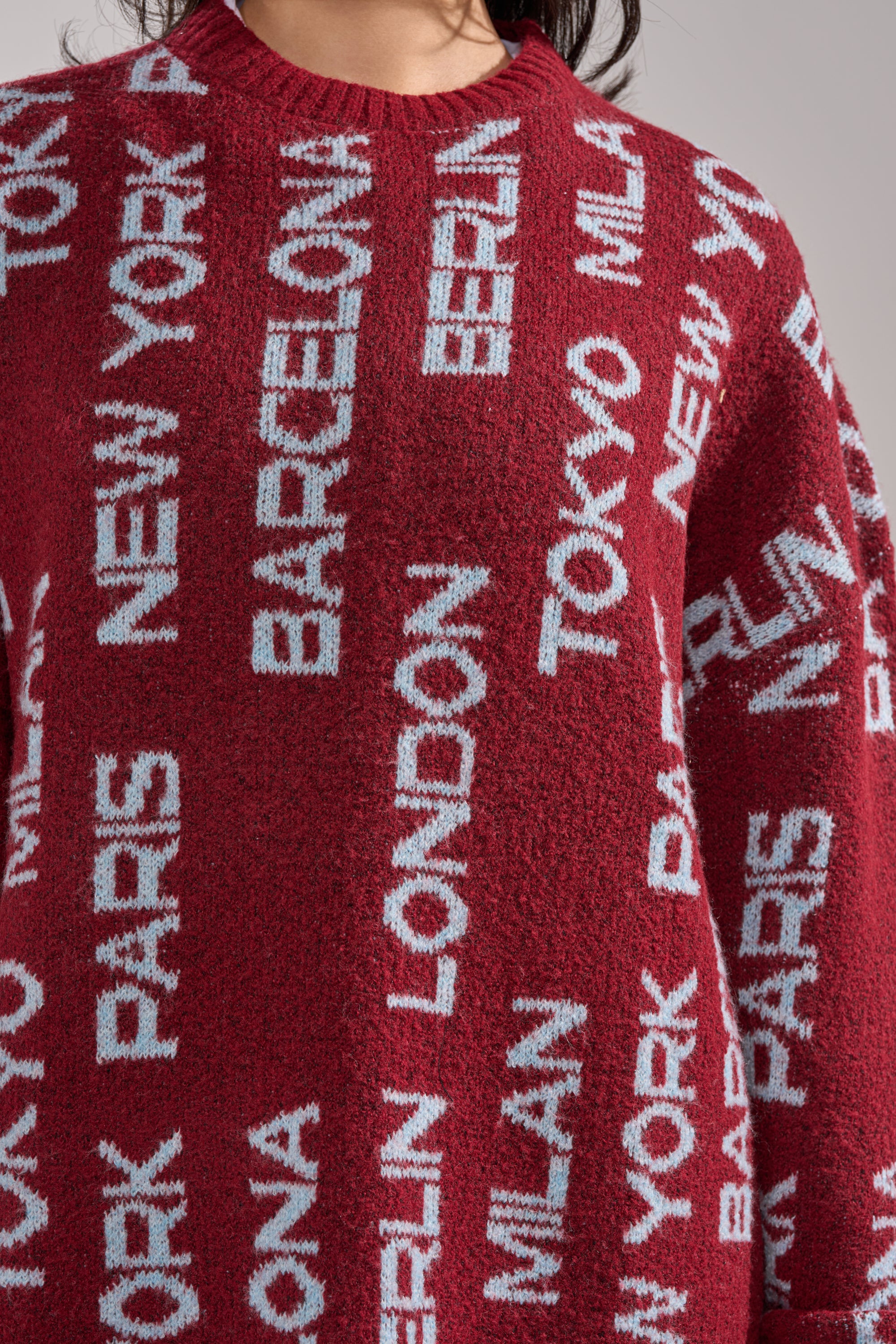 A person wearing the AROUND THE WORLD SWEATER MINI DRESS IN RED, a cozy piece with light blue city names like New York, Paris, and Tokyo in a bold, repeating pattern—perfect for standout winter style on chilly days. 7
