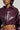 A person wearing the NATALIA CROCODILE PU BUTTON DOWN SHIRT in dark purple, featuring a crocodile pattern and a cropped silhouette, reveals a hint of midriff. Large silver hoop earrings accentuate the look against a plain, light-colored background.