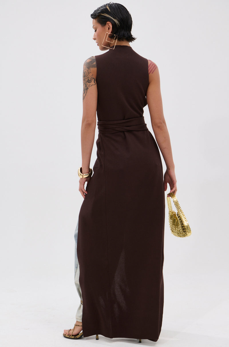 A person with short dark hair faces away, wearing the OVER THE TOP CUTOUT SWEATER IN CHOCOLATE BROWN, gold hoop earrings, bracelets, and holding a small gold handbag. A tattoo is visible on one arm against a plain white background. 4