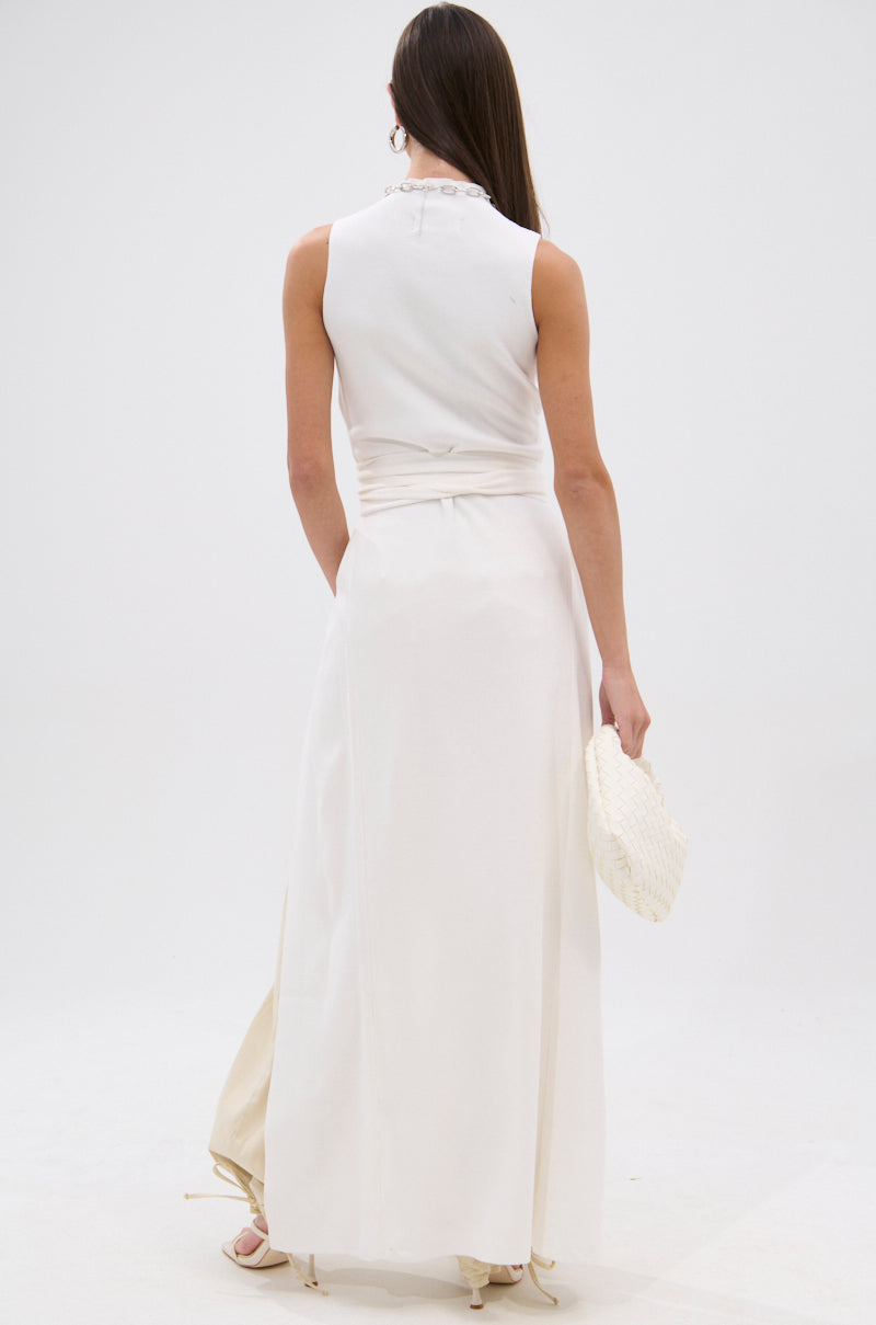 A woman faces away, wearing the OVER THE TOP CUTOUT SWEATER. She pairs it with a textured white clutch and heeled sandals against a plain white background. 3