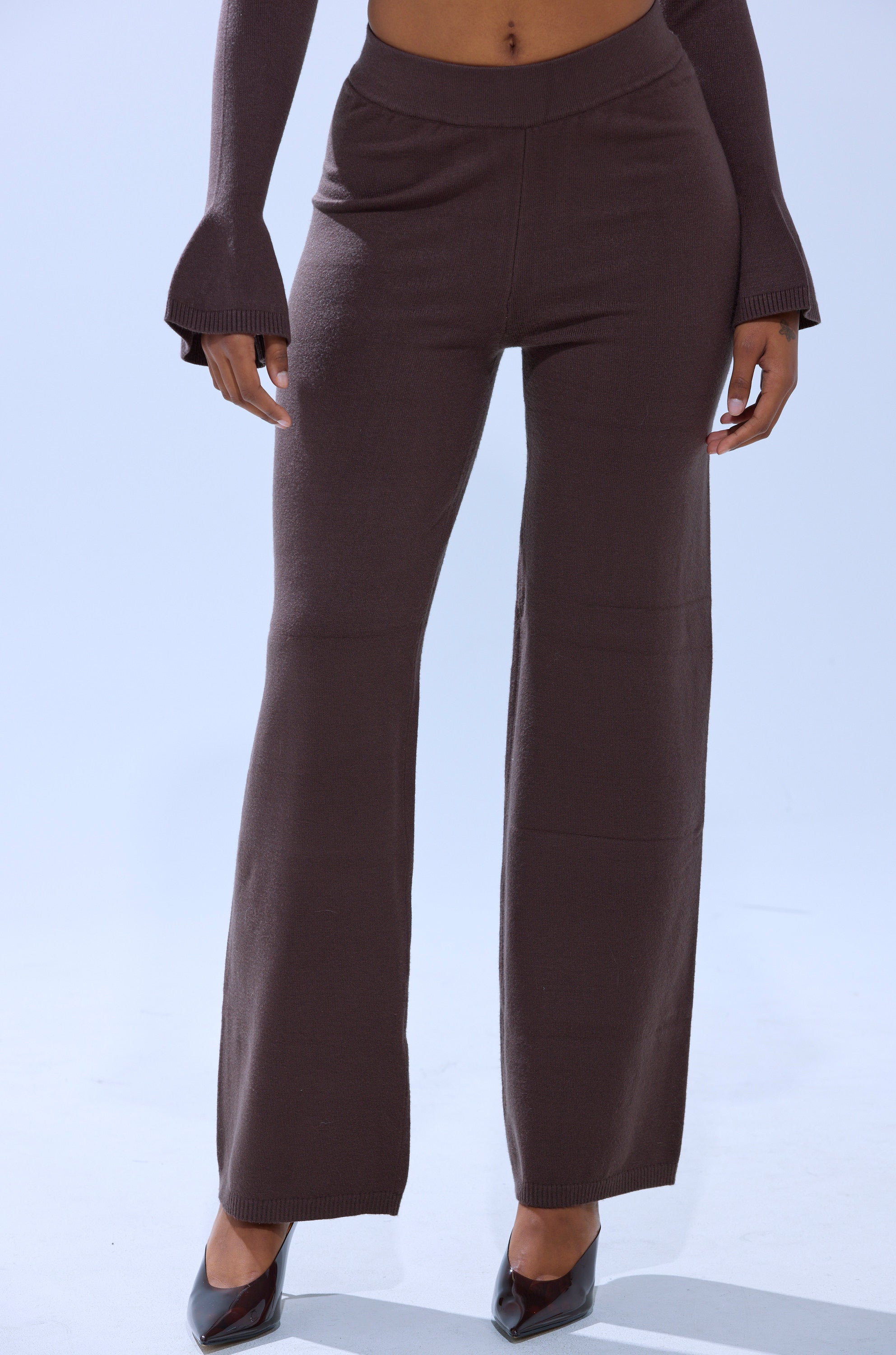 A person wearing the GET COZY WITH ME WIDE LEG PANT in brown, styled with dark pointed-toe heels and a matching long-sleeve top, stands against a plain light background. 1