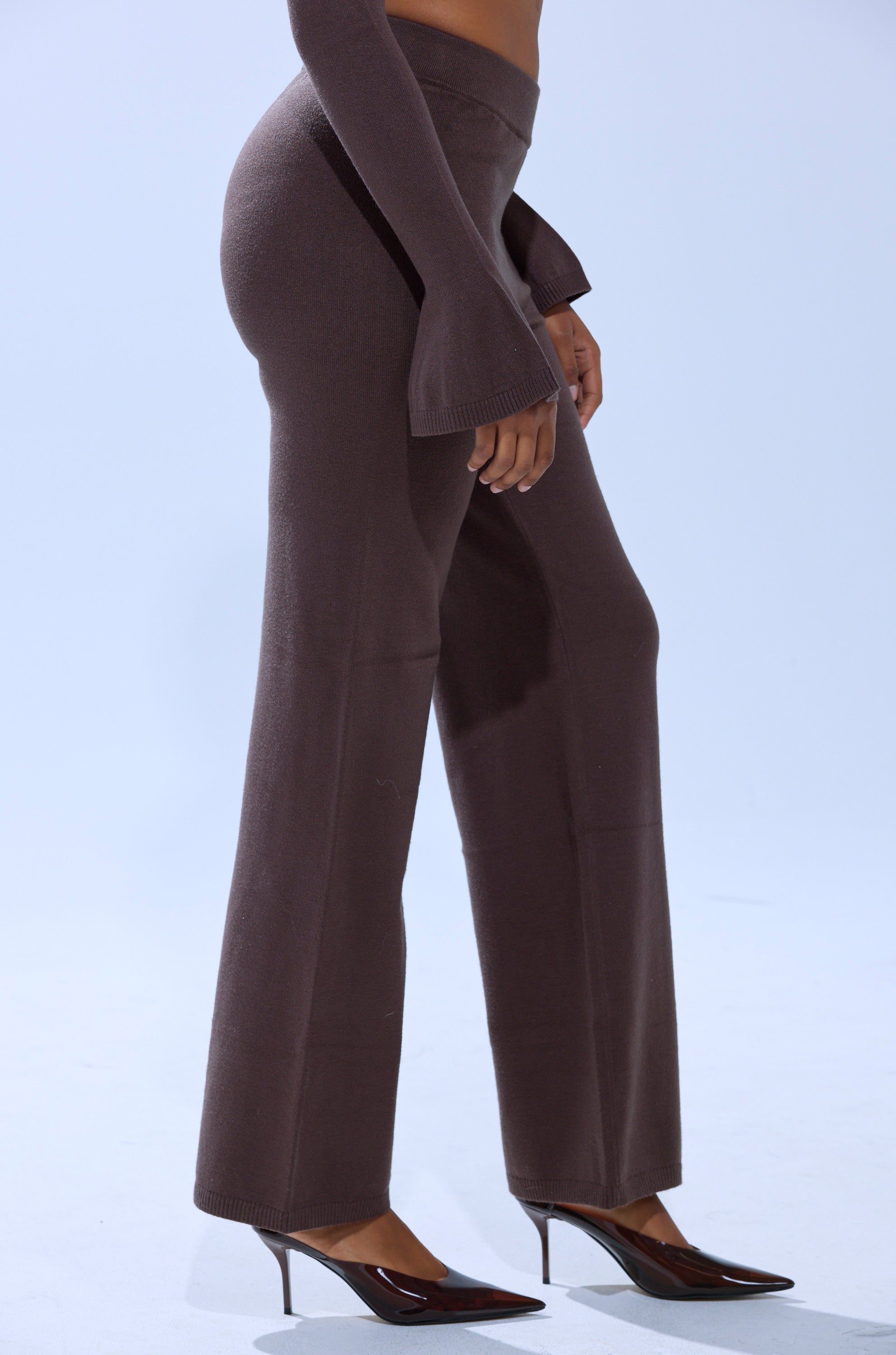 Wearing the GET COZY WITH ME WIDE LEG PANT, a person pairs these high-waisted, wide leg knit pants with a matching long-sleeve top and black pointed-toe heels, standing against a plain light background. 2