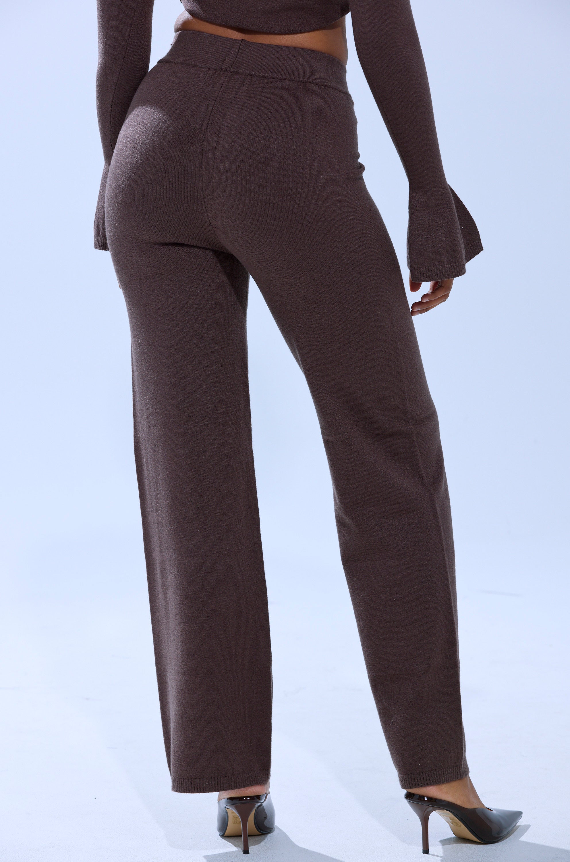 A person wearing the GET COZY WITH ME WIDE LEG PANT in brown and a matching long-sleeve top with flared cuffs, styled with high heels, stands with their back to the camera against a light background. 3