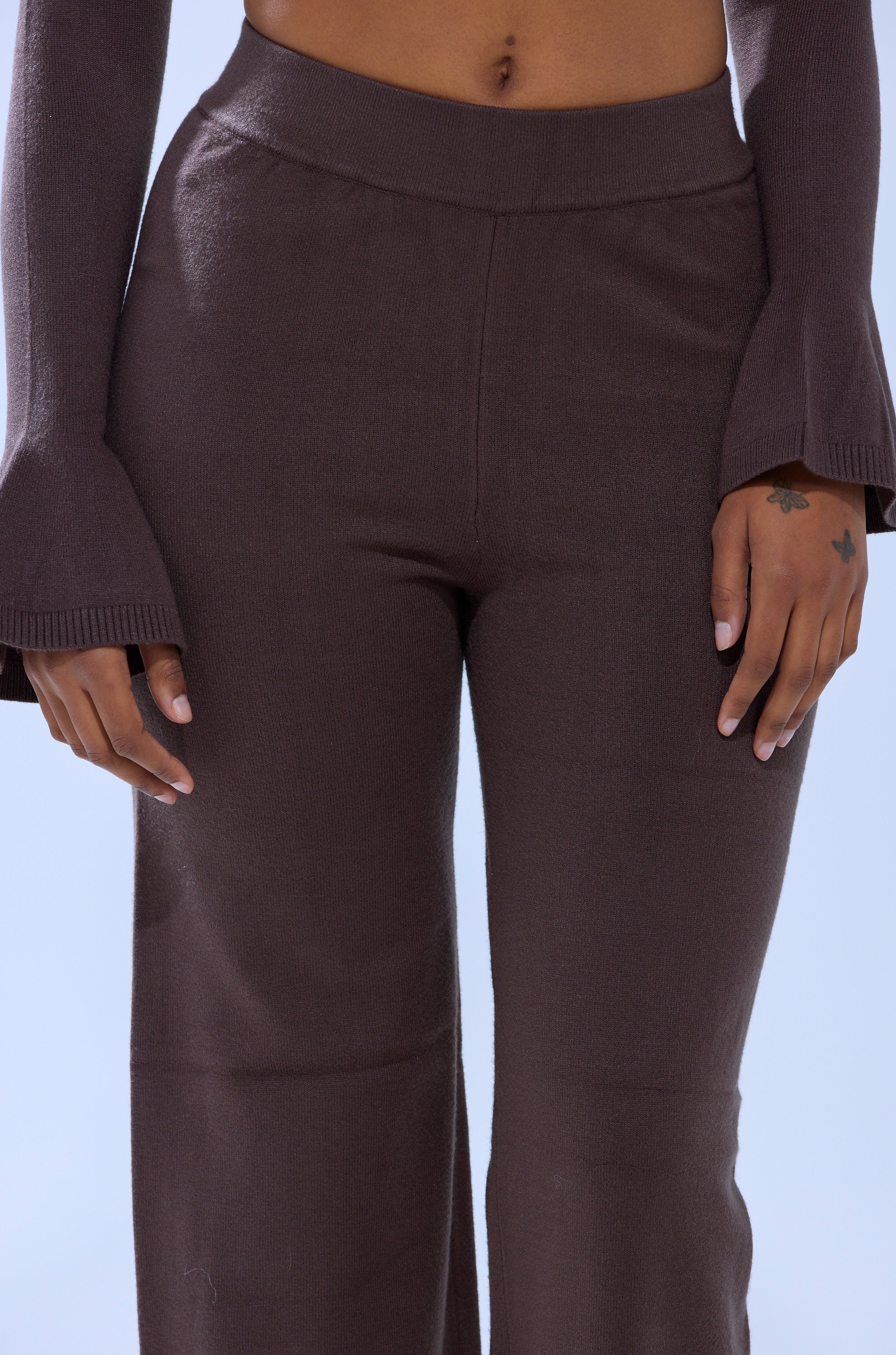A person wears the GET COZY WITH ME WIDE LEG PANT—high-waisted, brown, stretchy knit—with a matching long-sleeve top with flared cuffs, hands by their sides. The wide leg silhouette pops against a light blue background. 6
