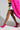 A person confidently strides, wearing a bright pink faux fur coat, an abstract-patterned skirt, and AZALEA WANG ROMEE FUCHSIA PONY HAIR PUMPS with pointed toes. The image highlights their legs and the coat's dynamic hem against a neutral background, showcasing the vibrant ensemble.