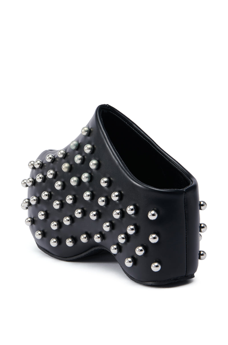 A close-up view of the avant-garde AZALEA WANG ROMESCO BLACK EMBELLISHED CLOG with a unique sculptural design. The clog is adorned with evenly spaced metallic studs covering its faux leather surface. Its platform sole and absence of a visible heel lend it an abstract, futuristic appearance.
